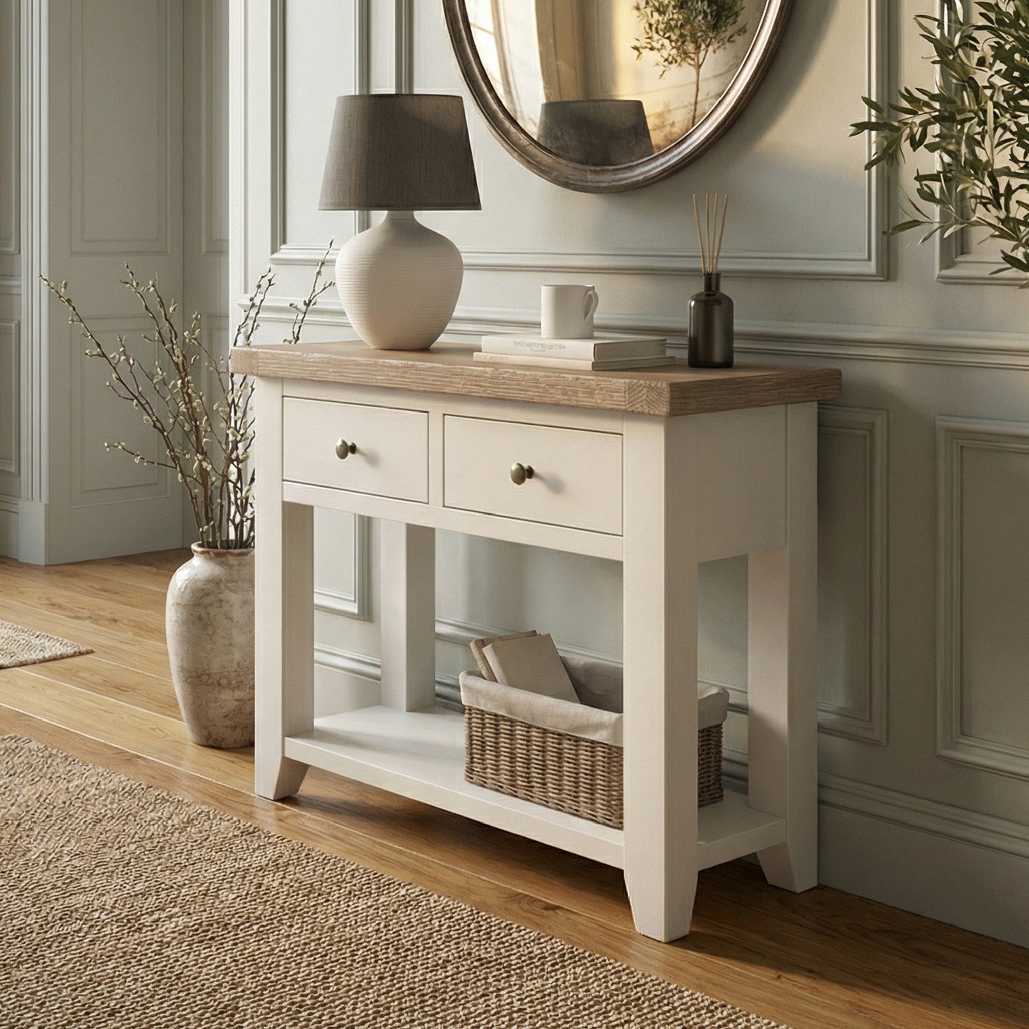 Burford 2 Drawers Console Table in Warm White, styled with a lamp, vase, and basket in a bright room with wooden floors.
