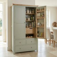 The Burford Double Larder Unit in Sage Green stands open in a bright kitchen, displaying jars, bottles, and drawers—an ideal oak top storage solution.