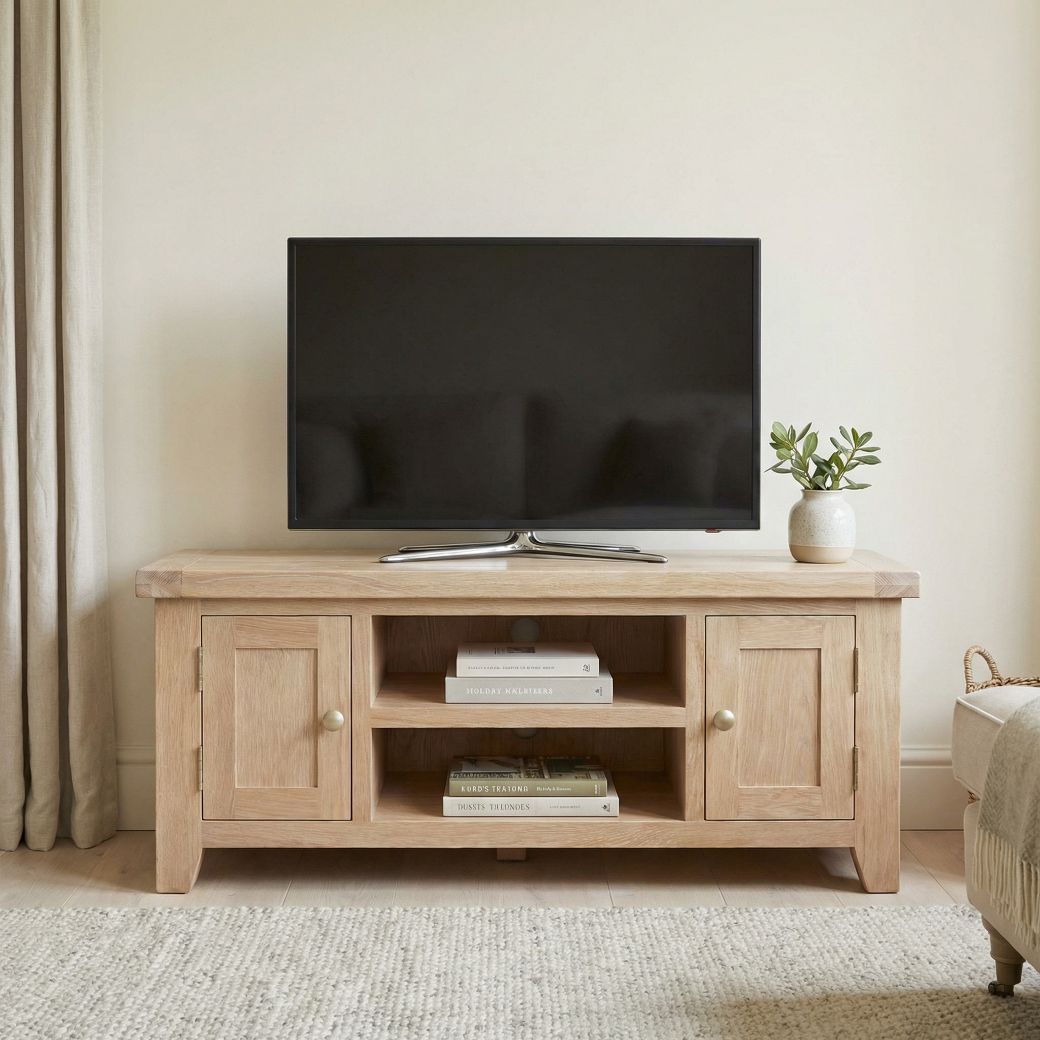 The Burford 120cm Media Unit in Natural Oak displays a flat-screen TV, complemented by books and a plant, all set in a neutral, cozy room.