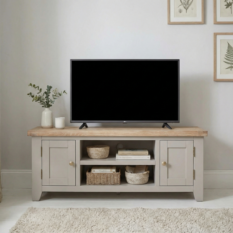 A flat-screen TV on a Burford 120cm Media Unit in Pebble Grey, styled with baskets, books, and a vase, sits against a light wall.