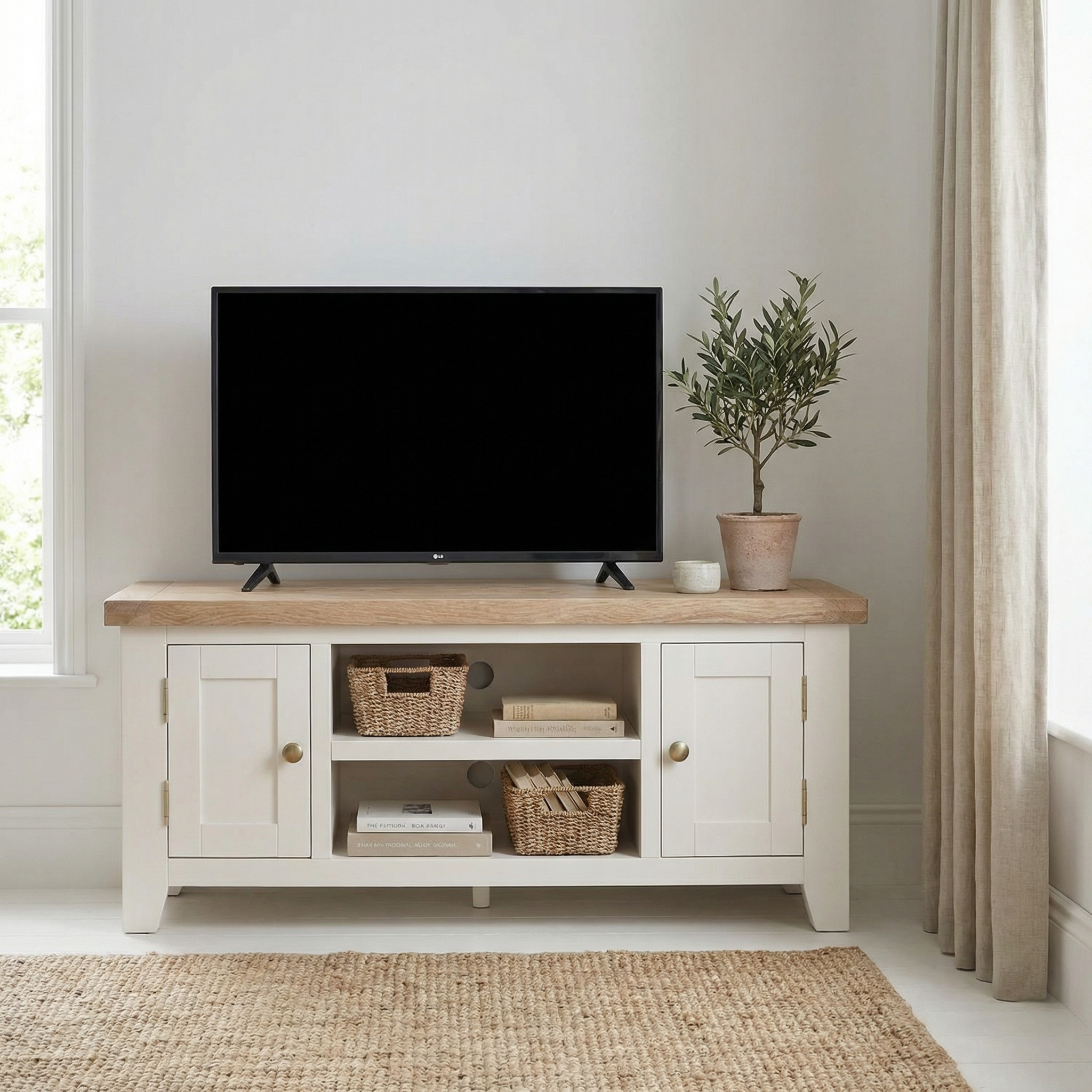 A TV sits on a Burford 120cm Media Unit in Warm White with baskets and a potted plant, in a bright, minimalist living room featuring white-washed oak accents and painted cabinets.