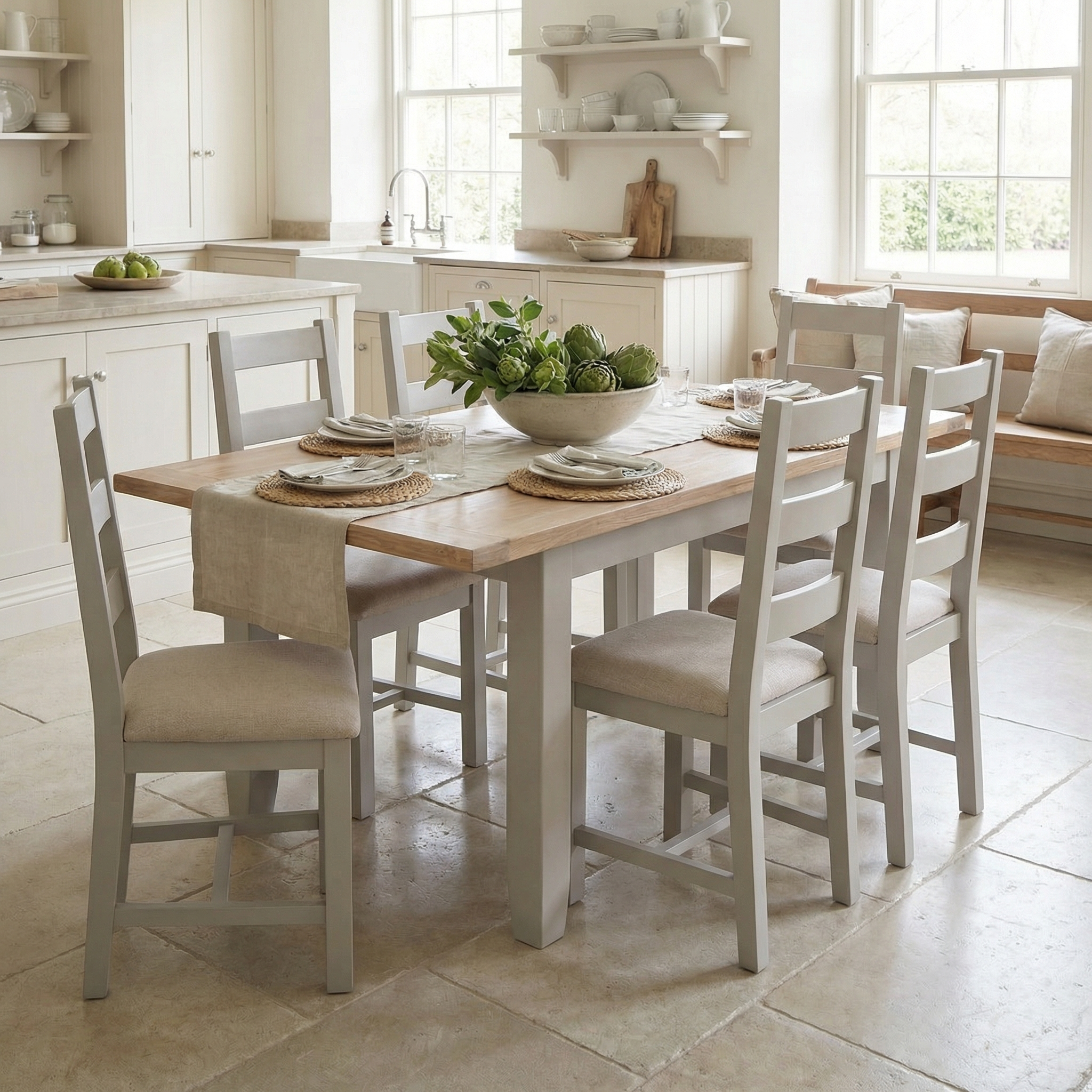 The Burford 6 Seat Extending Dining Set in Pebble Grey, styled with a table runner and a bowl of artichokes, sits elegantly on a stone floor.
