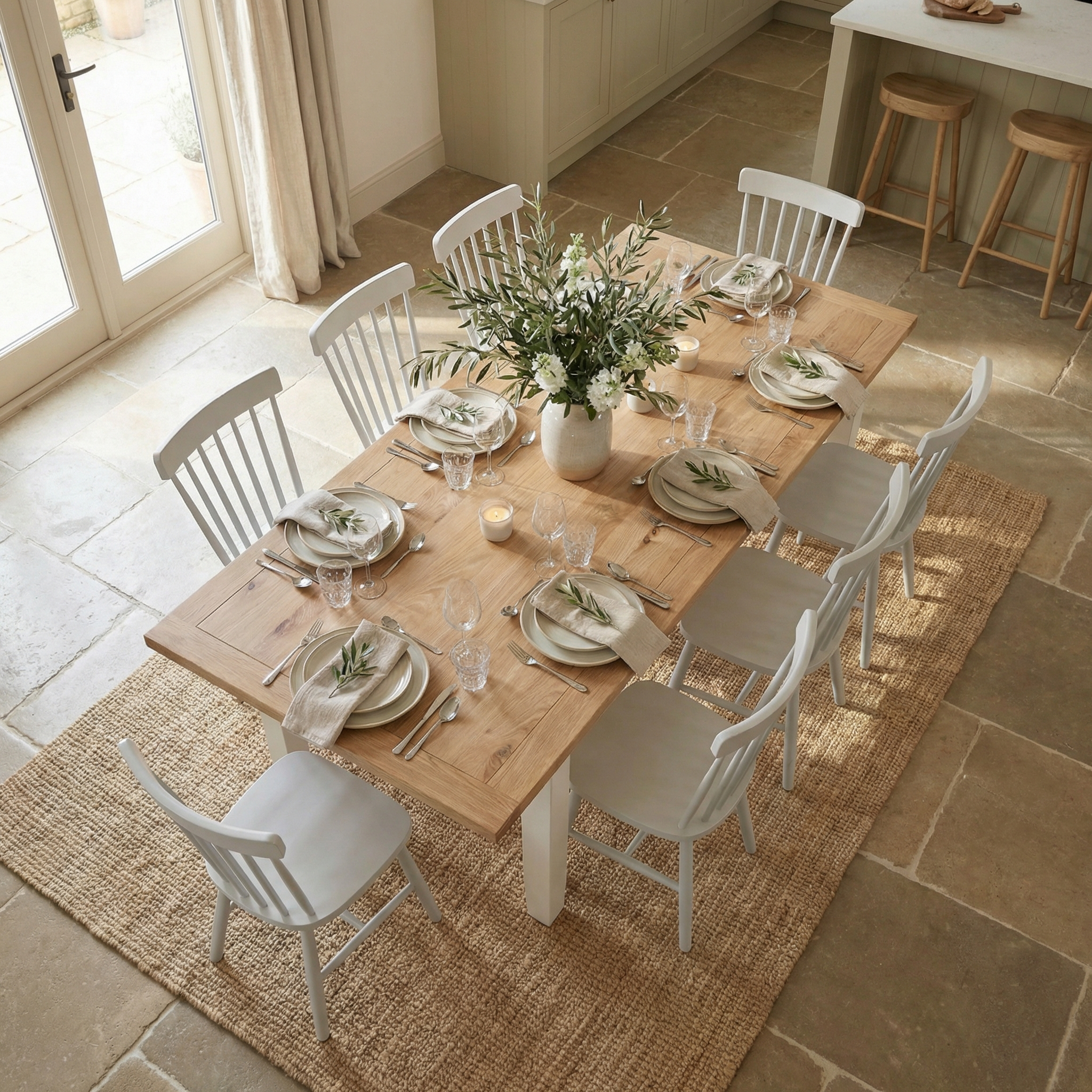 The Burford 8 Seat Extending Dining Set with Spindleback Dining Chair in Warm White, styled with plates, glasses, and a floral centerpiece, creates an inviting dining area for eight.