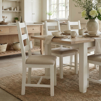Bright kitchen with a wooden table, flowers, neutral decor on a woven rug, and Burford Set of 2 Ladderback Dining Chairs with Fabric Seat in Warm White.