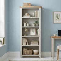 A Burford Large Bookcase in Pebble Grey, filled with books, baskets, decor, and plants, stands in a light modern room with blue walls and a nearby desk.