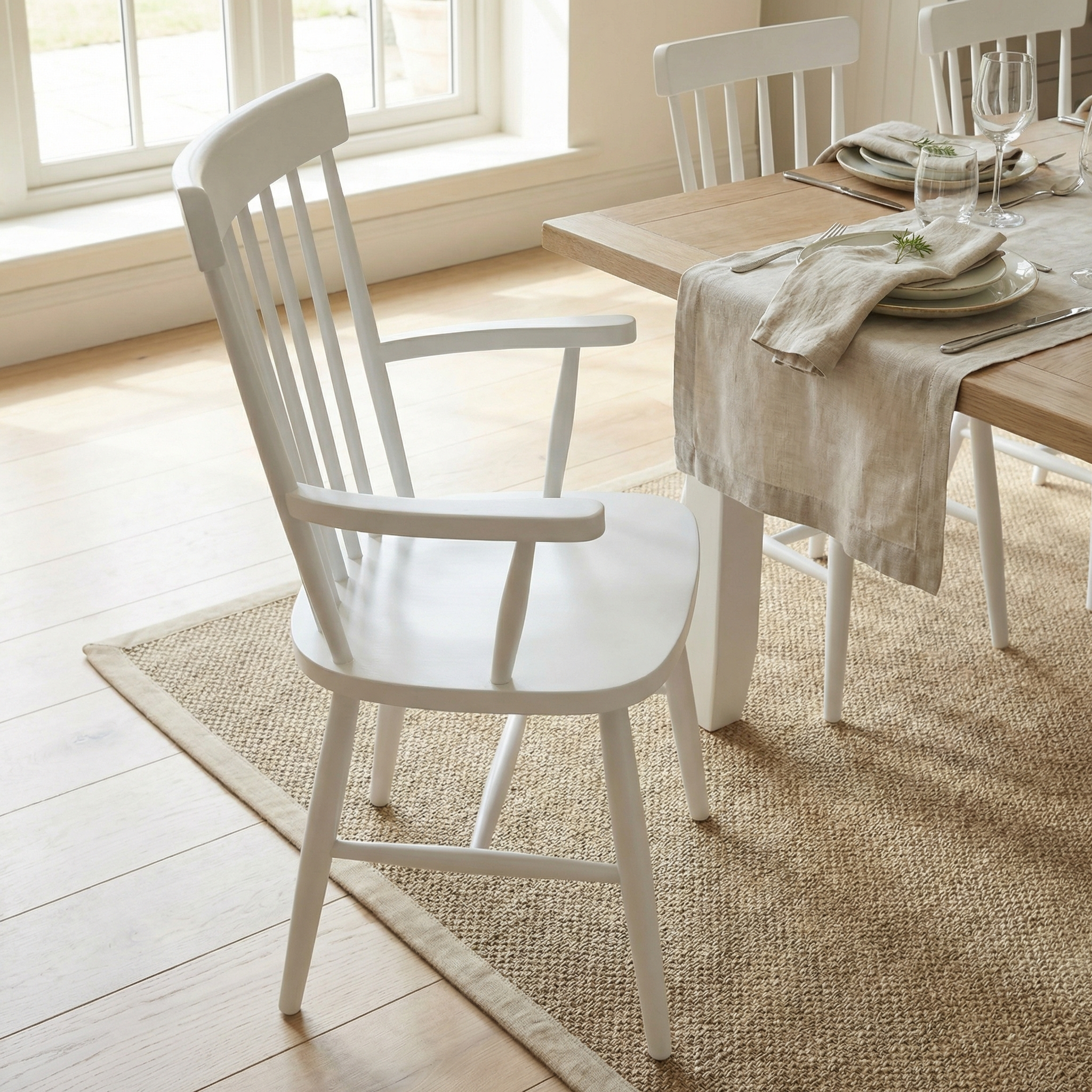 The Burford Spindleback Dining Chair with Armrest in Warm White adds charm to the cozy dining room set, perfectly matching the plates and glasses on the table.