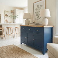 The Burford Large 3 Door 3 Drawers Sideboard in Navy Blue pairs with two lamps, neutral decor, and bar stools to enhance a bright, airy living space.