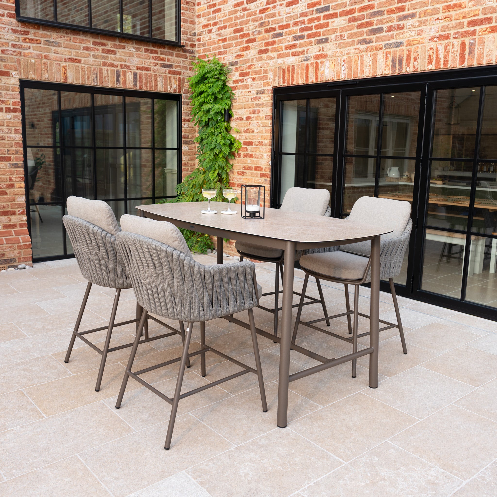 The Capri 4 Seat High Rectangular Dining Set in Stone Grey features four cushioned chairs and a stylish table, perfect for modern patios or dining spaces with ample natural light.