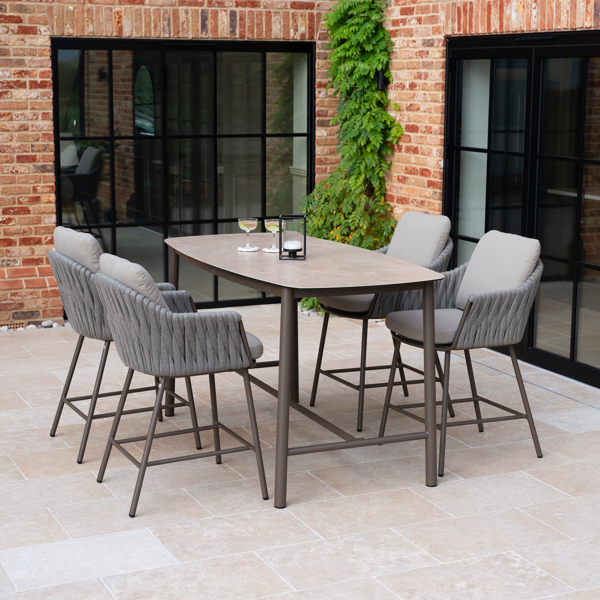 The Capri 4 Seat High Rectangular Dining Set in Stone Grey offers four cushioned chairs and a stylish table, ideal for outdoor dining on patios near glass doors or brick walls.