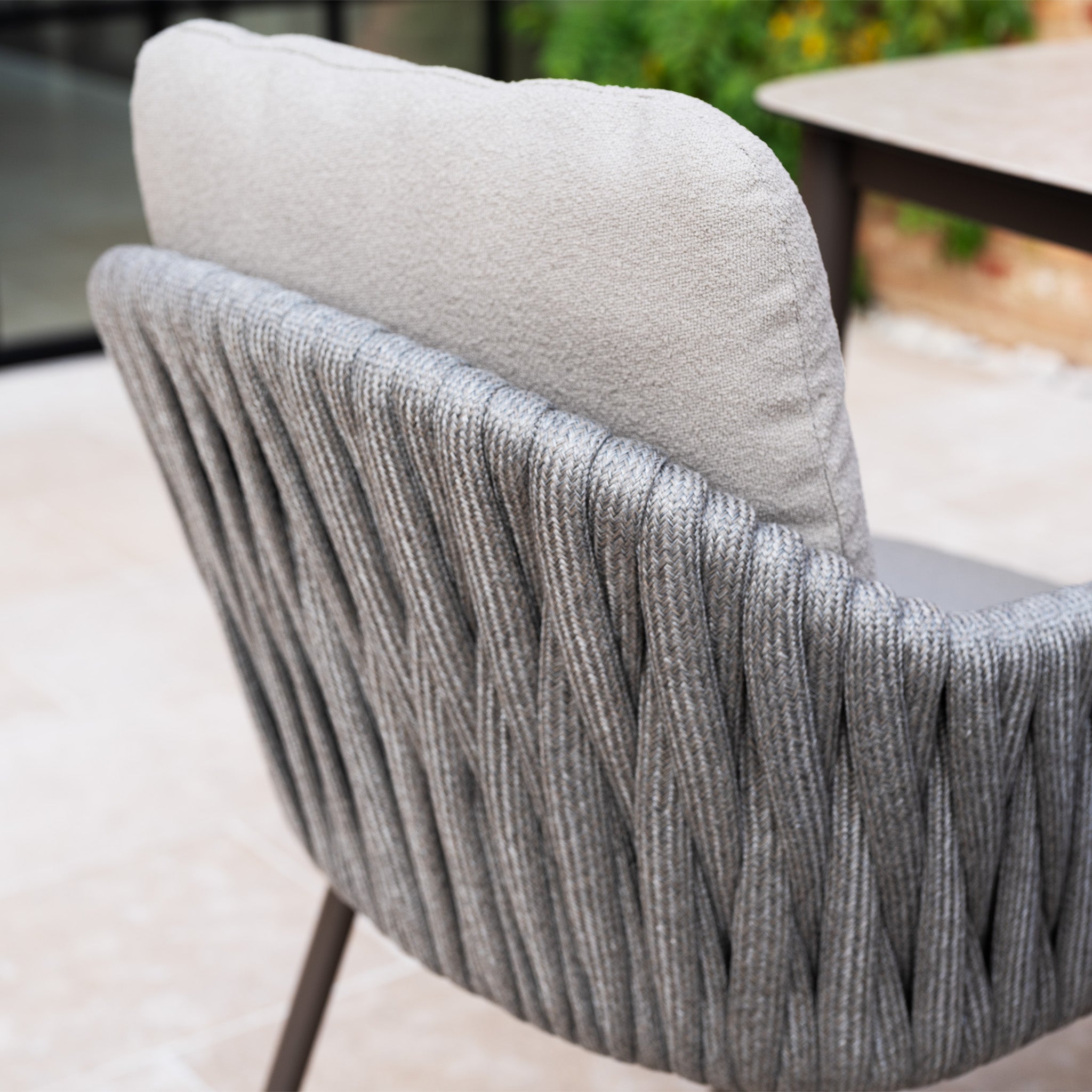Close-up of a modern chair from the Capri 4 Seat High Rectangular Dining Set in Stone Grey, featuring a woven gray backrest and a light cushion—ideal for contemporary outdoor spaces.