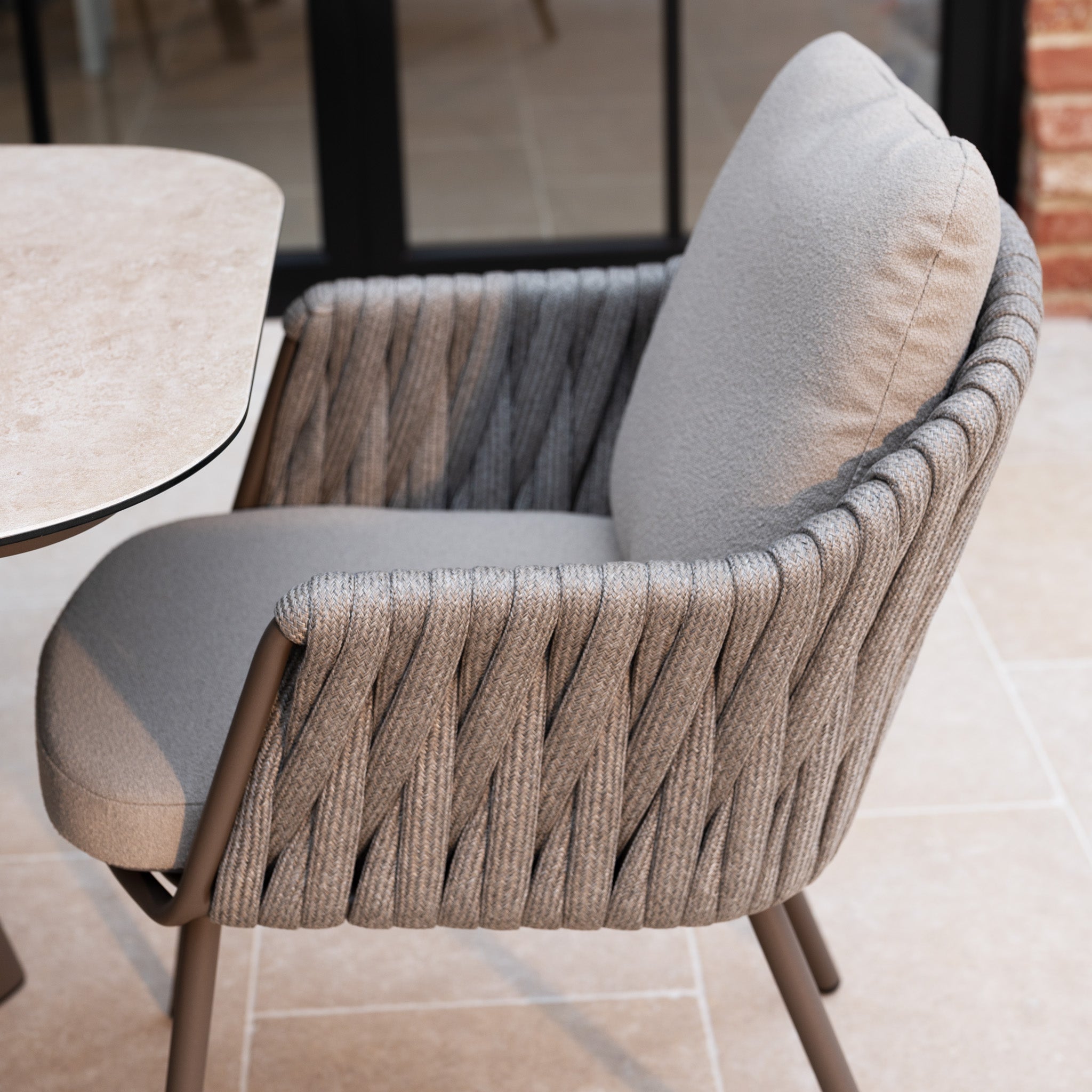 The Capri 6 Seat Curved Rectangular Dining Set in Stone Grey features stylish, modern woven chairs and a stone table, bringing comfort and elegance to your tiled patio for outdoor dining.