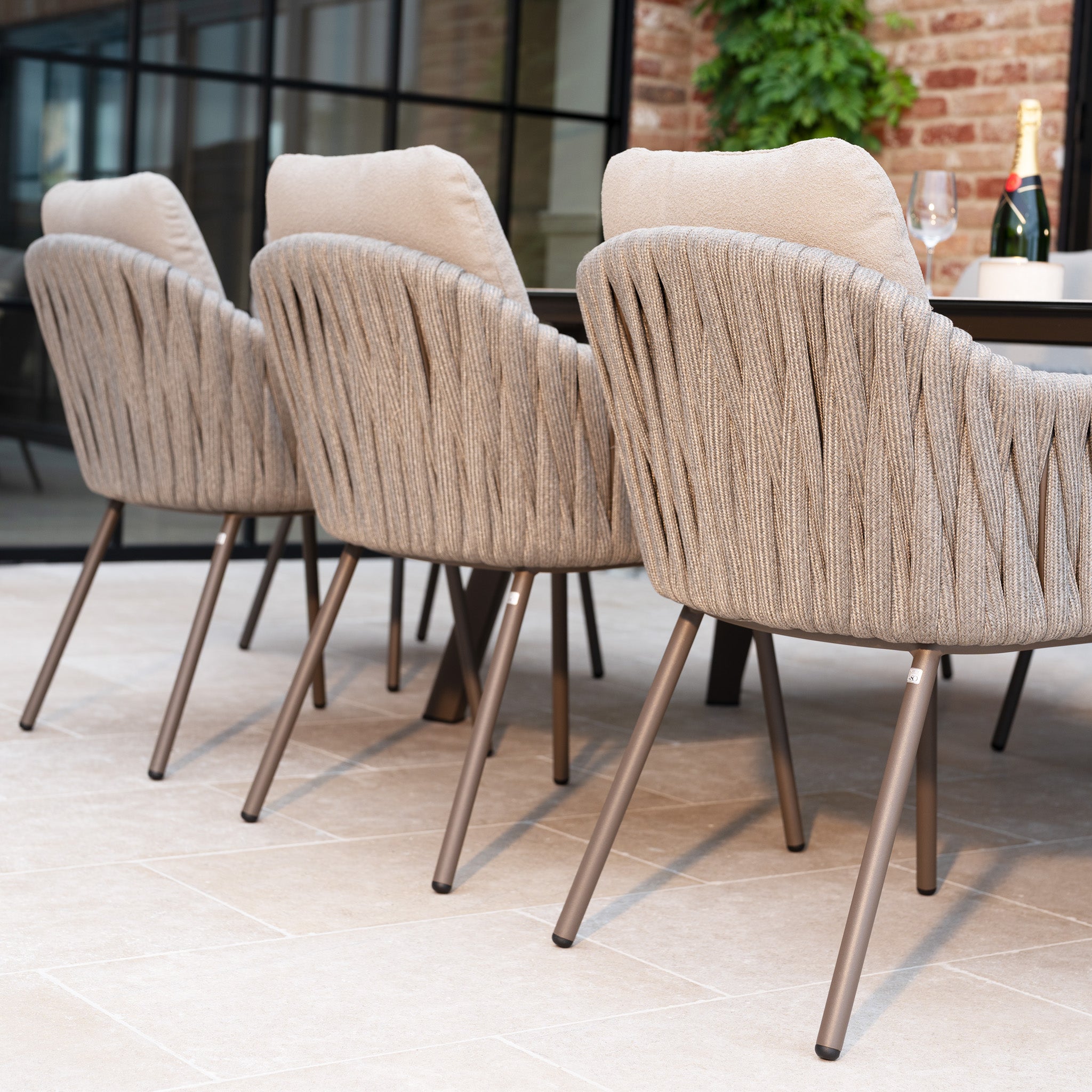 Three modern beige chairs with metal legs are lined up by a table on a tiled patio, creating a stylish setting that perfectly complements the Capri 8 Seat Curved Rectangular Dining Set in Stone Grey.