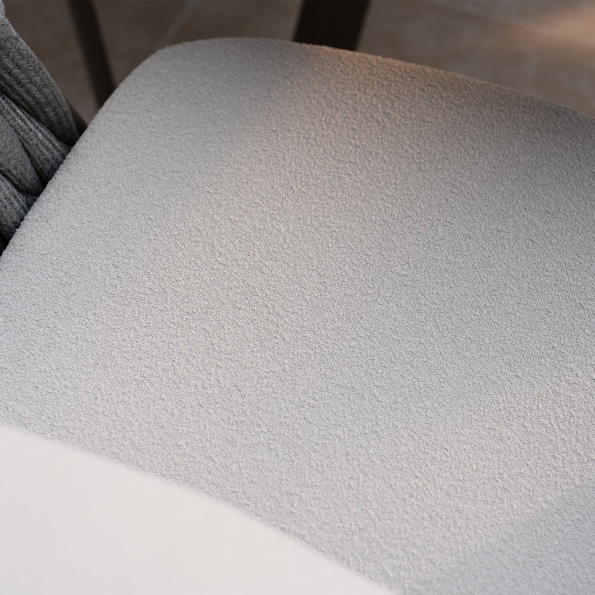Close-up of a textured light gray fabric seat cushion from the Capri 4 Seat High Rectangular Dining Set in Stone Grey, highlighted by soft sunlight and shadows.