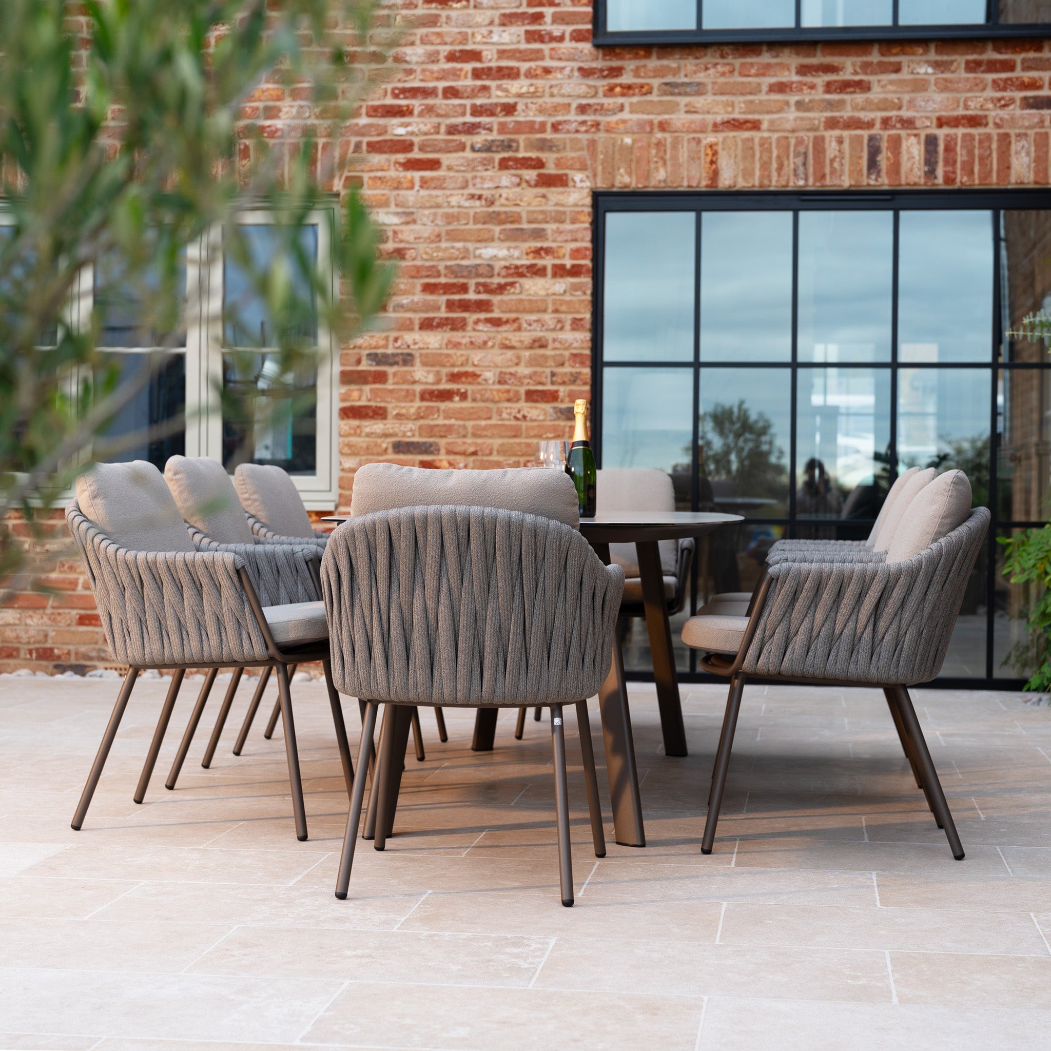 The Capri 8 Seat Curved Rectangular Dining Set in Stone Grey features cushioned chairs and a stylish table, perfect for outdoor spaces.