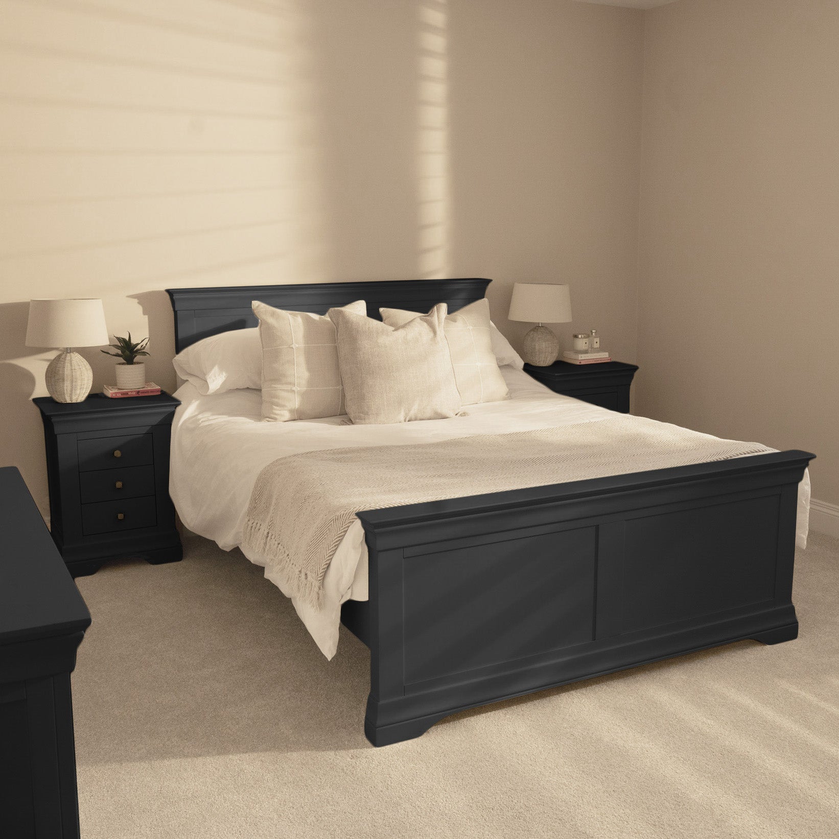 A modern bedroom features the Chalbury 5ft High-End Kingsize Bed Frame in Dusky Black, complemented by white bedding, two bedside tables, and beige walls with sunlight casting soft shadows.