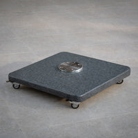 The Granite 90kg Cantilever Parasol Base With Wheels, featuring a central metal plate, rests on a tiled floor—ideal for stabilizing cantilever parasols.