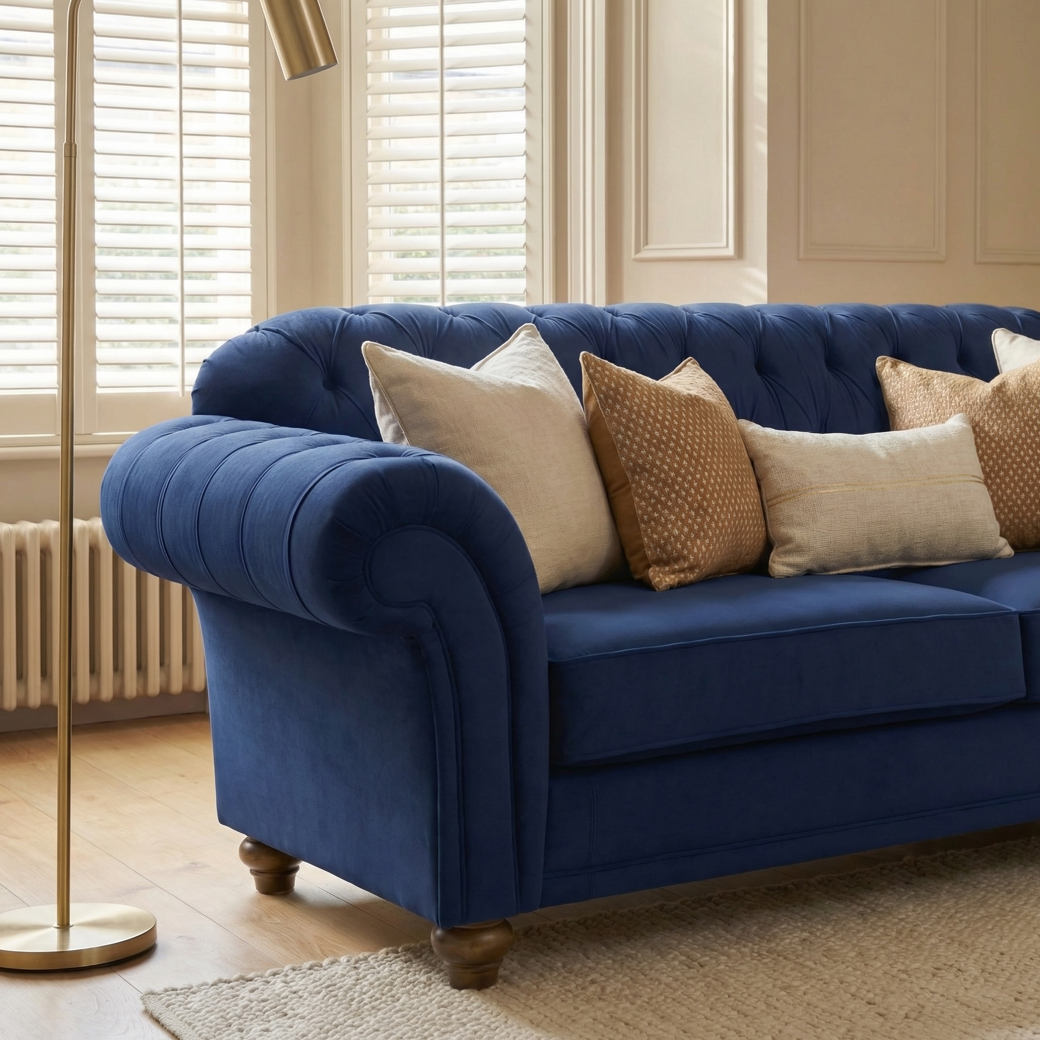 Chesterfield 2 Seat Velvet Sofa in Royal Blue with neutral and gold cushions in a bright living room with large windows and wooden floors.