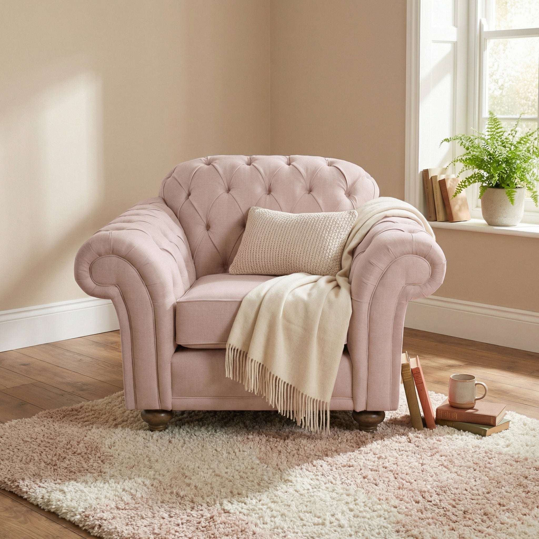 A Chesterfield Armchair in Dusky Pink, handmade in England and topped with a beige throw and pillow, sits beside a window.