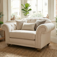 The Chesterfield Loveseat in Ivory with three cushions is handcrafted in England and sits in a bright, cozy living room filled with plants and large windows.