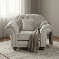 The Chesterfield Velvet Armchair in Feather Grey is paired with a cozy throw and pillow, set on a textured rug in a softly lit, neutral-toned room.