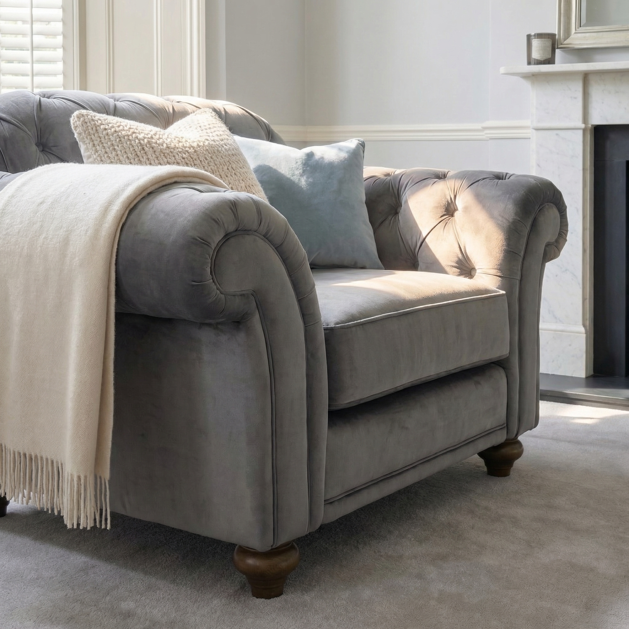 Chesterfield Velvet Armchair in Steel Grey with a cream throw and blue cushion in a bright, elegant living room.