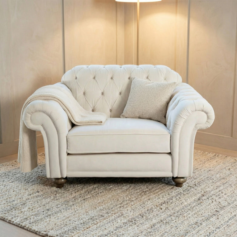 The Chesterfield Velvet Loveseat in Cream, paired with a pillow and blanket on a textured rug in soft lighting, brings handcrafted-in-England elegance to the room.