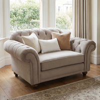 Chesterfield Velvet Loveseat in Mink shown with four throw pillows in a bright room featuring large windows and wooden floors.