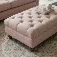 Chesterfield Footstool in Dusky Pink with wooden legs holds a tray with candles, placed on a patterned rug next to a matching sofa.