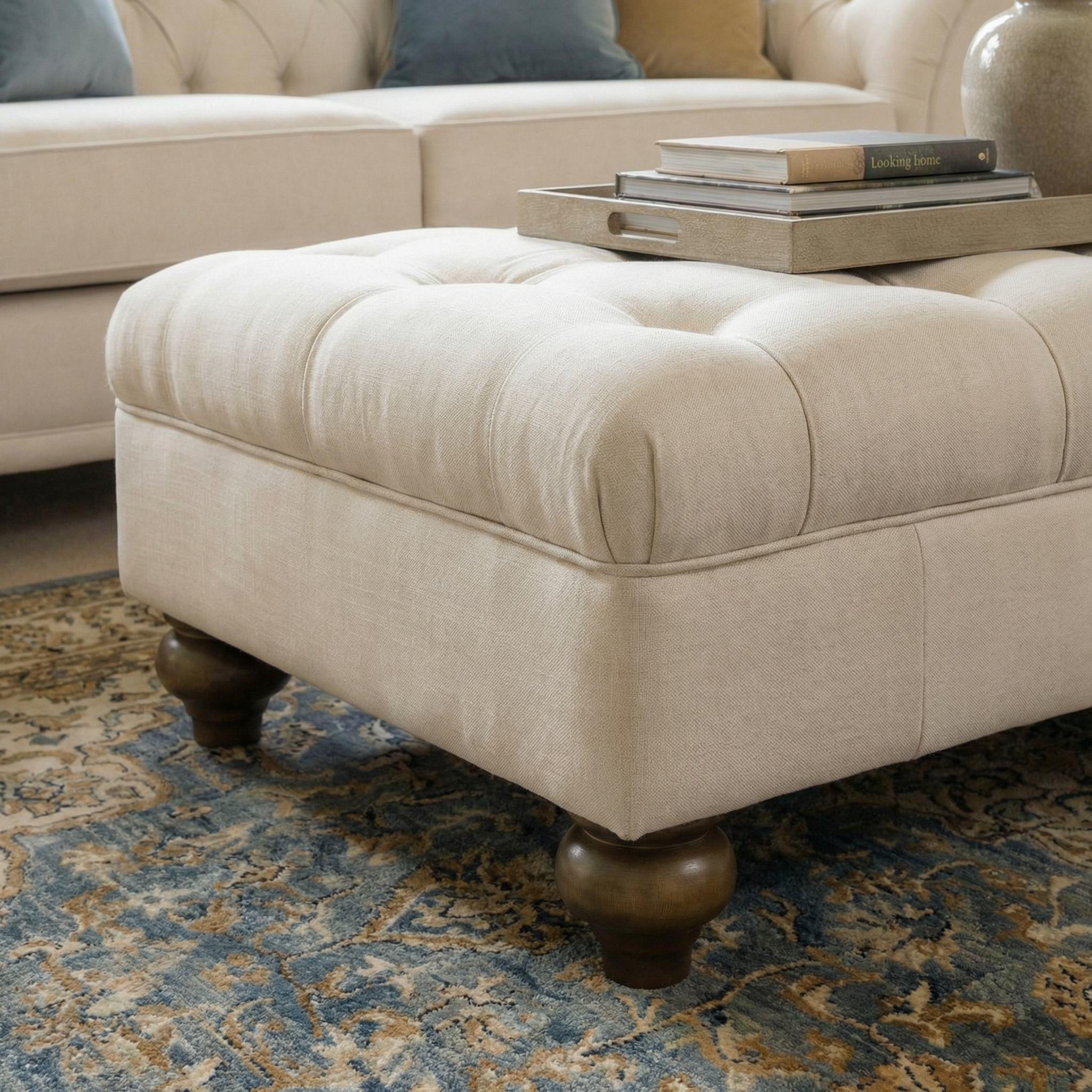 Chesterfield Footstool in Ivory with tufted design and wooden legs sits on a patterned rug, styled as an ottoman with books and a tray placed on top.