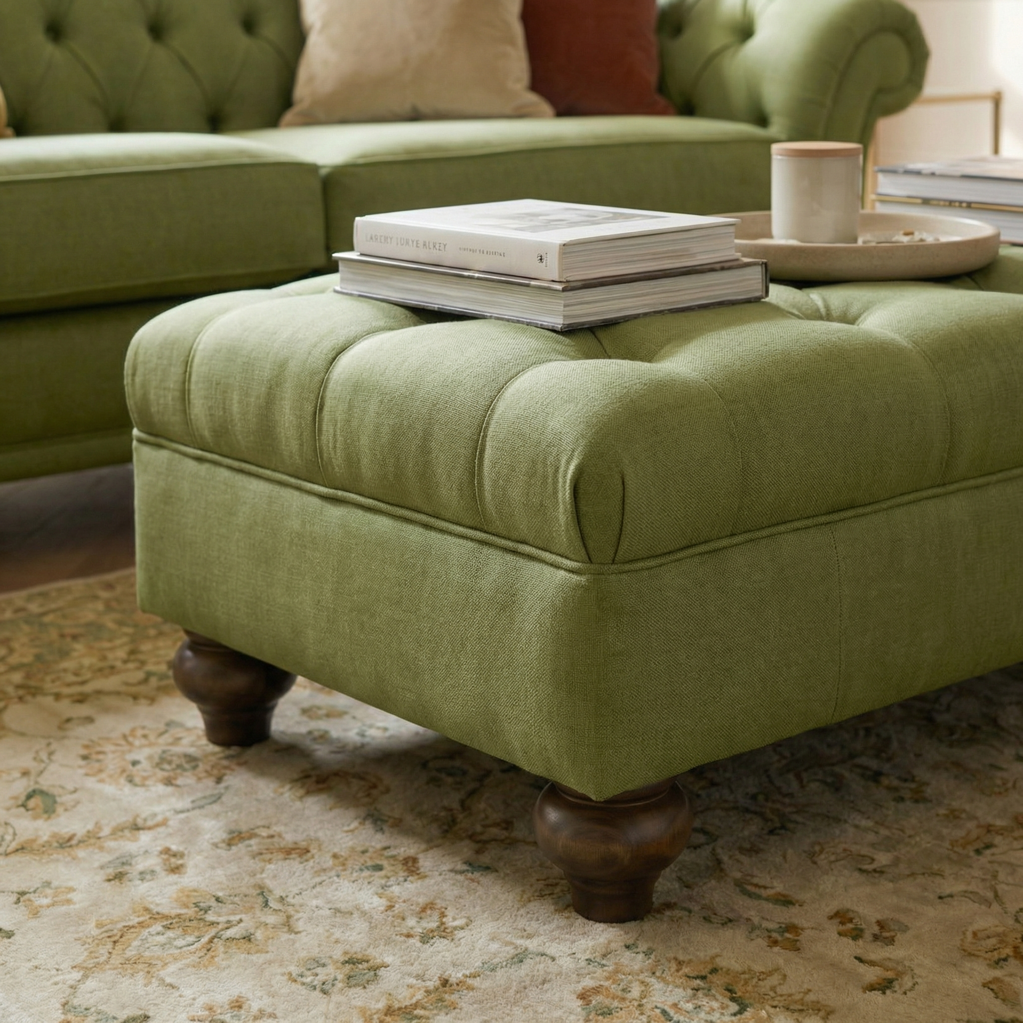 The Chesterfield Footstool in Olive sits beside a matching sofa on a patterned rug, styled with books, a cup, and a tray—an elegant piece to bring classic British flair to your luxury living space.