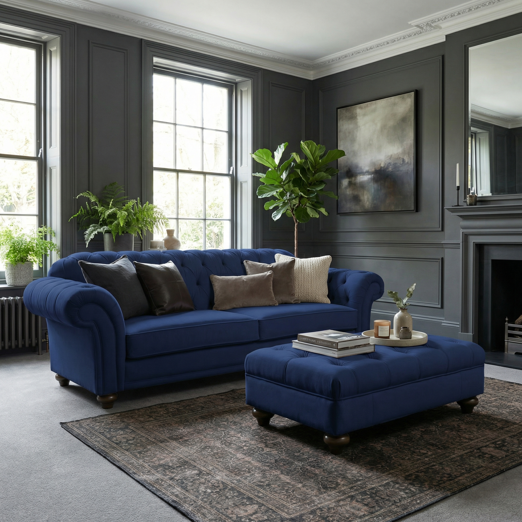 A modern living room with dark walls, plants, and large windows features a blue sofa and the Chesterfield Velvet Footstool in Royal Blue.