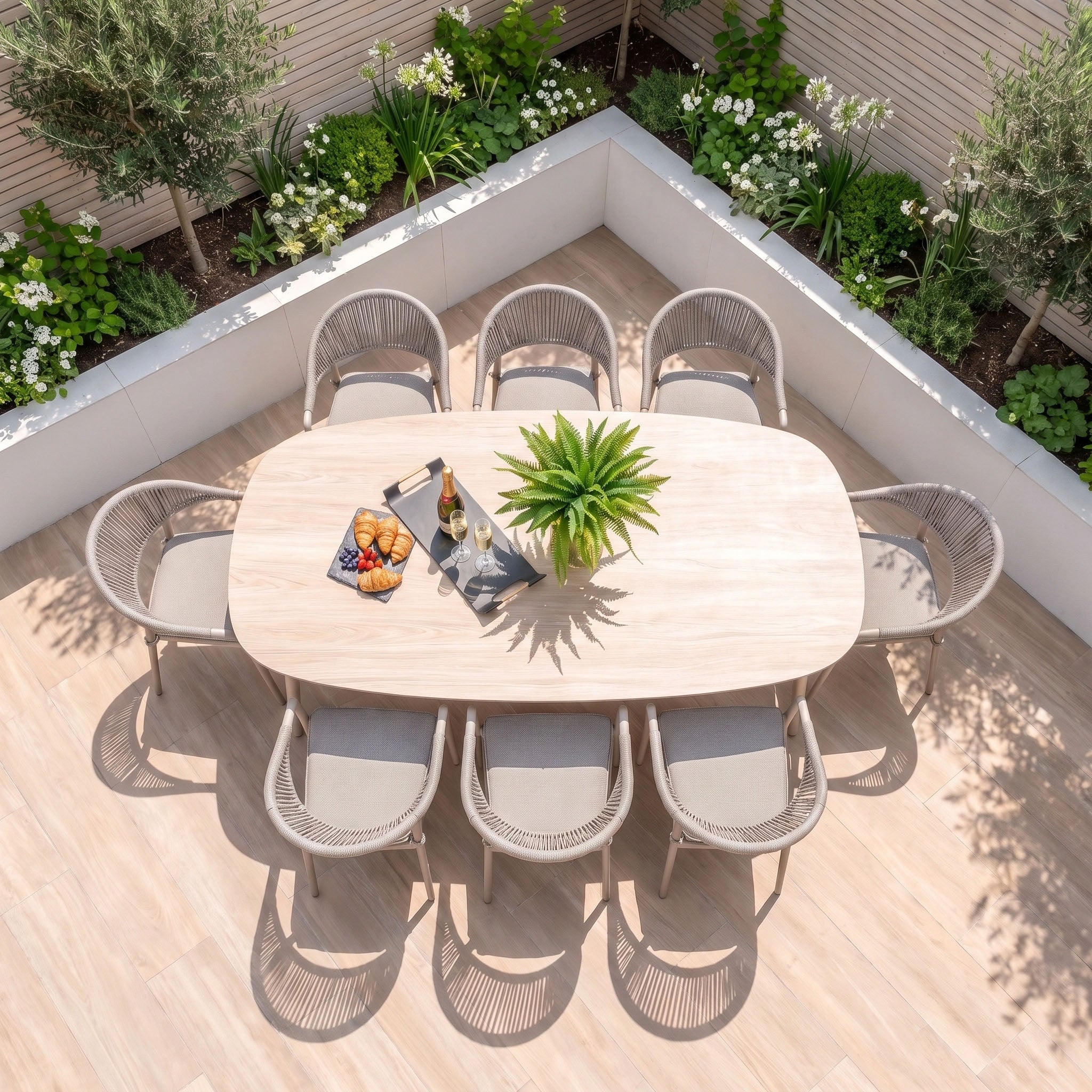 The Cloverly 8 Seat Dining Set with Albatross Oval Dining Table in Latte features an elegant aluminium garden furniture design, including a spacious oval table and eight comfortable chairs. Perfect for outdoor gatherings, the set is beautifully arranged with a plant centerpiece, snacks, and drinks, all surrounded by lush green plants.