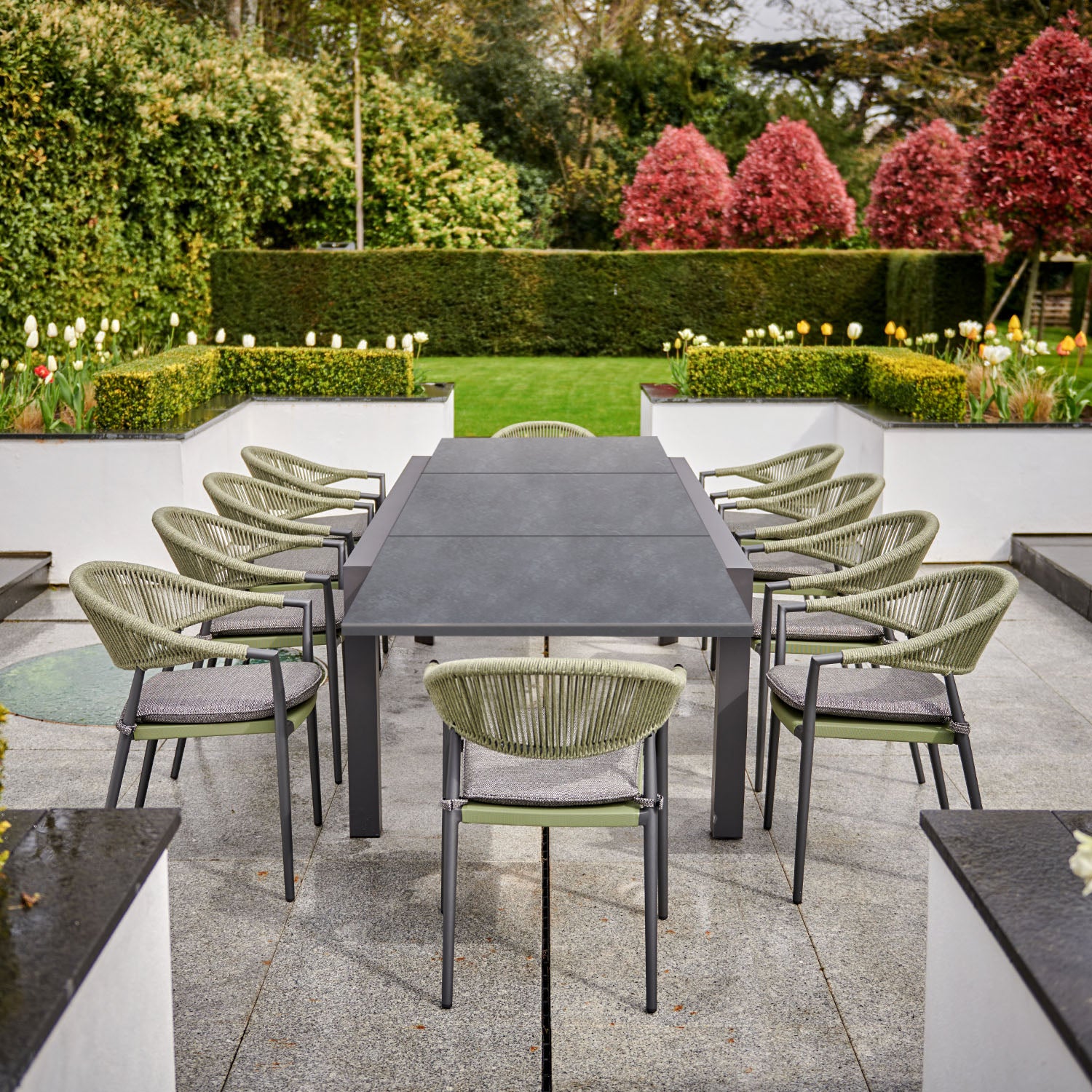 Cloverly 8 Seat Rectangular Extending Dining Set with a ceramic table in olive green, surrounded by a well-manicured garden.