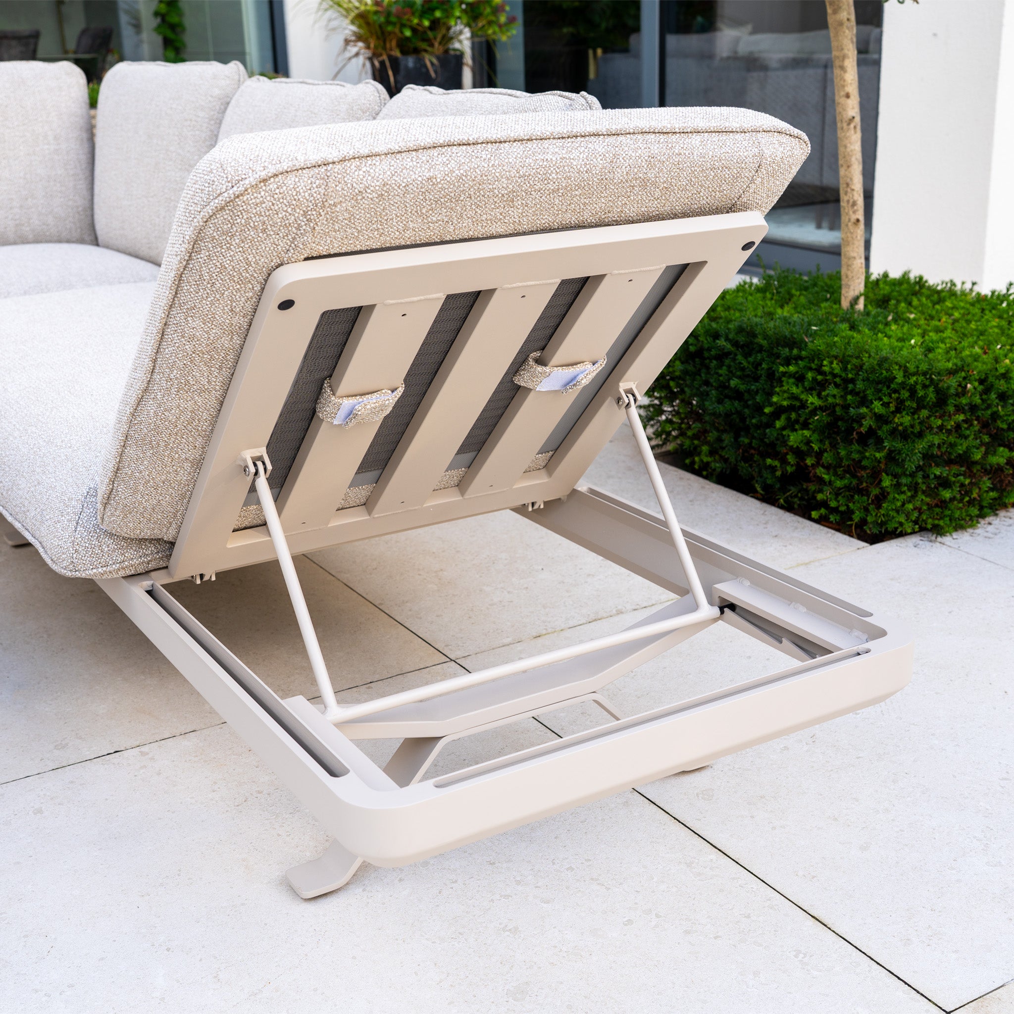 The Como Corner Sofa Set with Altura Rising Table in Oatmeal features open under-seat storage and is ideal for a tiled patio near greenery, offering versatile outdoor living with its adjustable aluminium table.