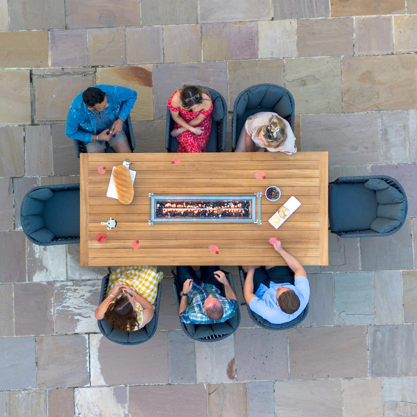 Top view of six people sitting around a Monterrey 8 Seat Rope Rectangular Teak Firepit Dining Set in Grey, featuring a rectangular table with a central fire pit and surrounded by elegant Outdoor Rope Fabric chairs.