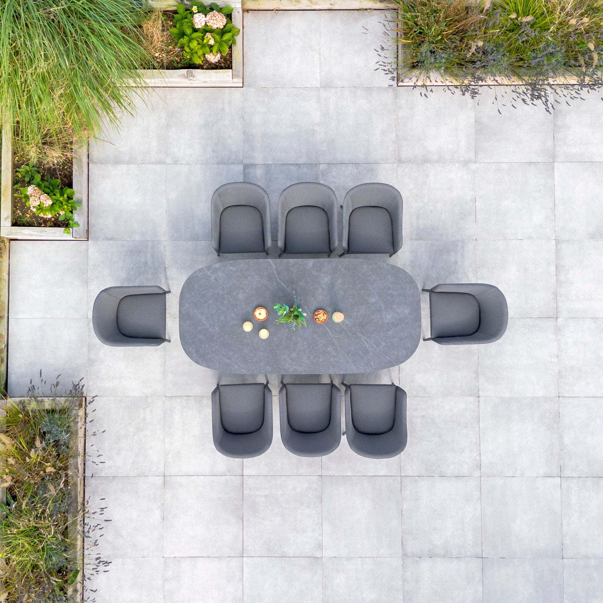 Luna 8 Seat Outdoor Fabric Oval Ceramic Dining Set in Grey with eight chairs, featuring durable all-weather material and Luna outdoor fabric, surrounded by greenery on a large, tiled patio.