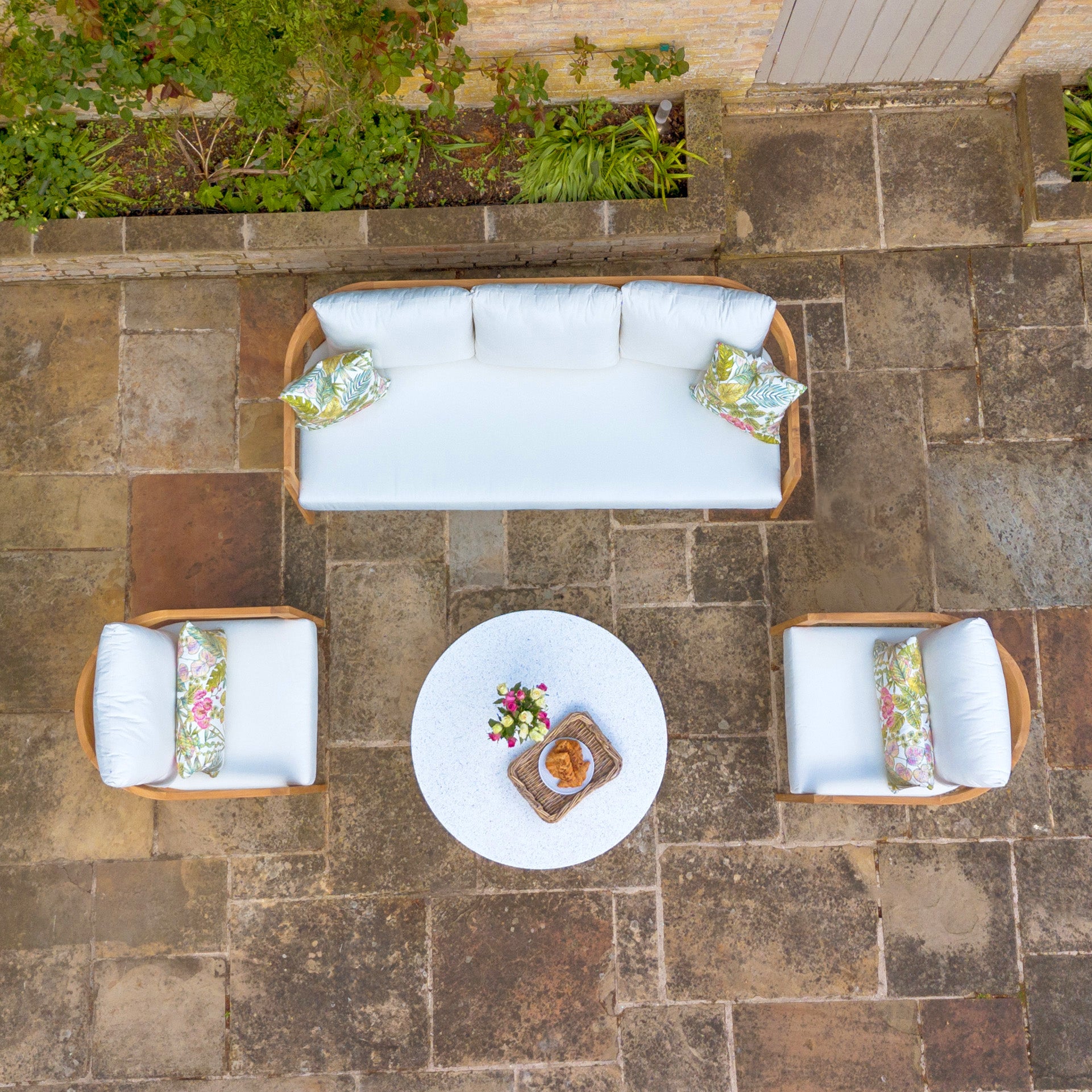 Outdoor seating area featuring the Yosemite 3 Seat Sofa Set in Glacier with a white cushioned sofa, two chairs, and a round coffee table crafted from sustainably sourced premium teak wood on a stone patio.