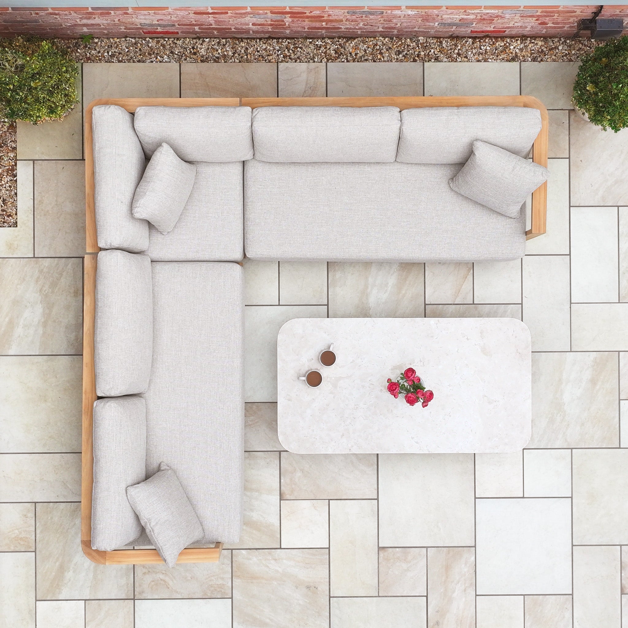 The Tivoli Corner Set with Marble Coffee Table in Fawn, seen from above, features an L-shaped design with a rectangular marble table, two cups, and a plant.