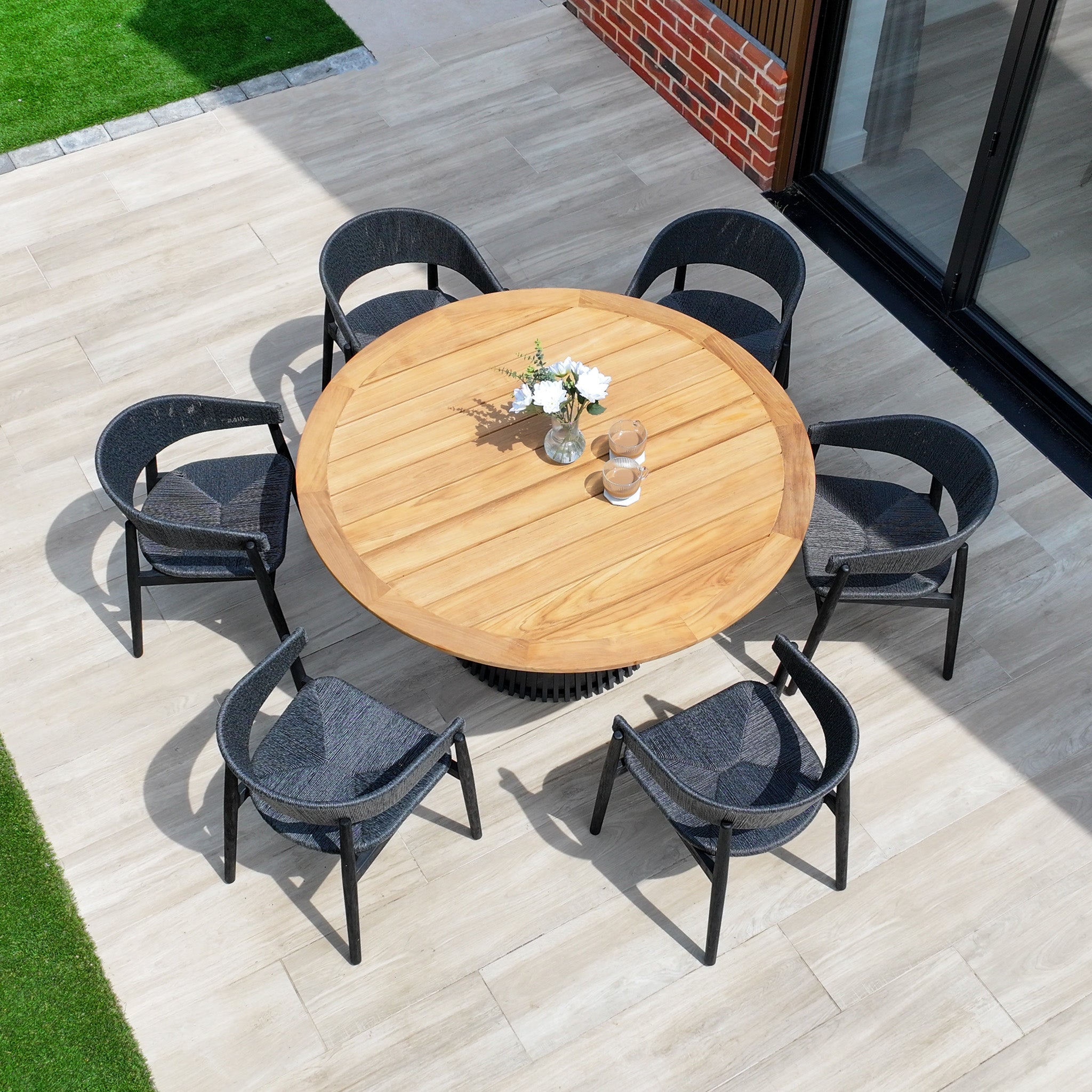 The Lucca 6 Seat Dining Set with Teak Round Table in Black is an inviting patio ensemble, perfect for gatherings, featuring a round teak table and six black chairs—ideal for stylish outdoor dining.