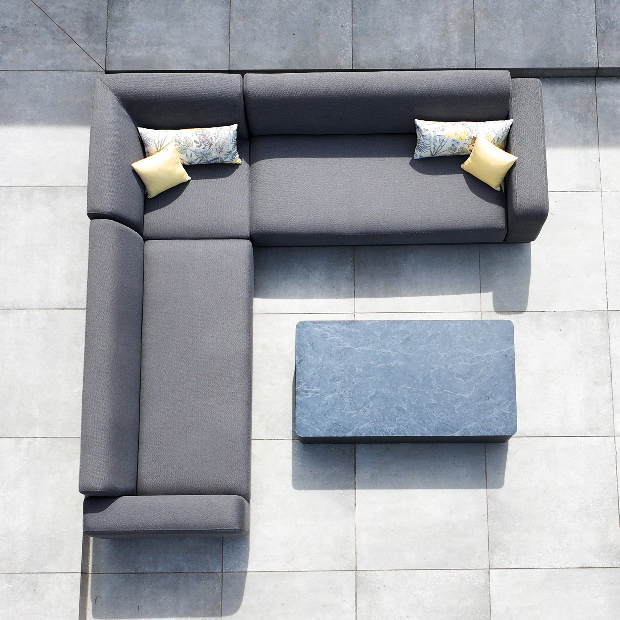 The Luna Outdoor Fabric Corner Sofa Set with Coffee Table in Grey is seen from above, featuring an L-shaped all-weather design, four cushions, and a rectangular coffee table on a tiled floor.