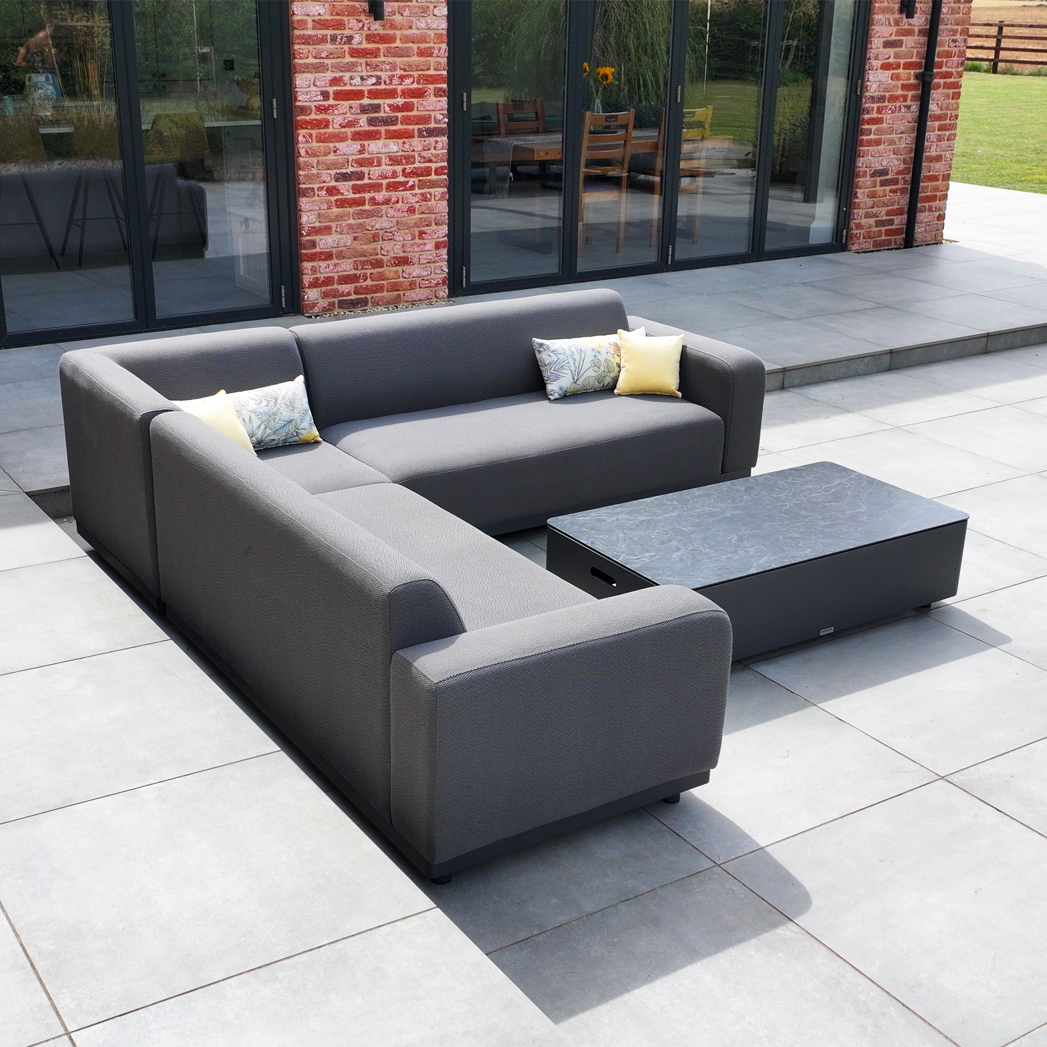 Luna Outdoor Fabric Corner Sofa Set with Coffee Table in Grey on a tiled patio in front of large windows.