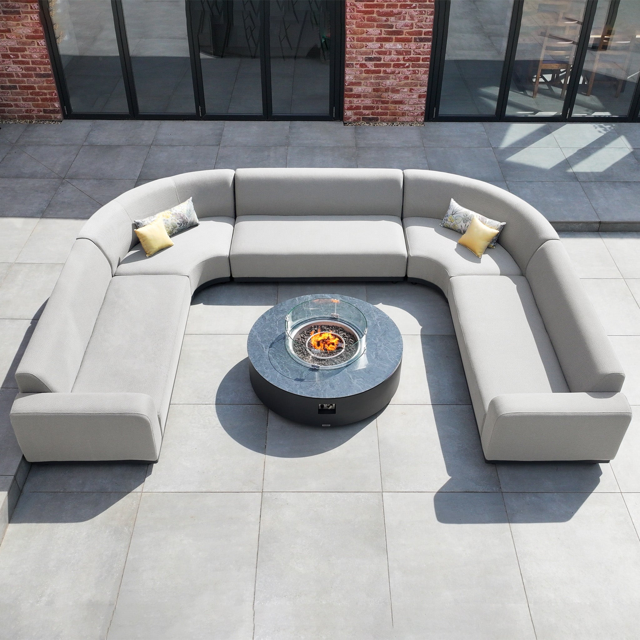 The Luna U-Shape Outdoor Fabric Curved Corner Group with Round Firepit Coffee Table in Oyster Grey offers a cozy, curved sectional and firepit table, ideal for outdoor gatherings on your patio.