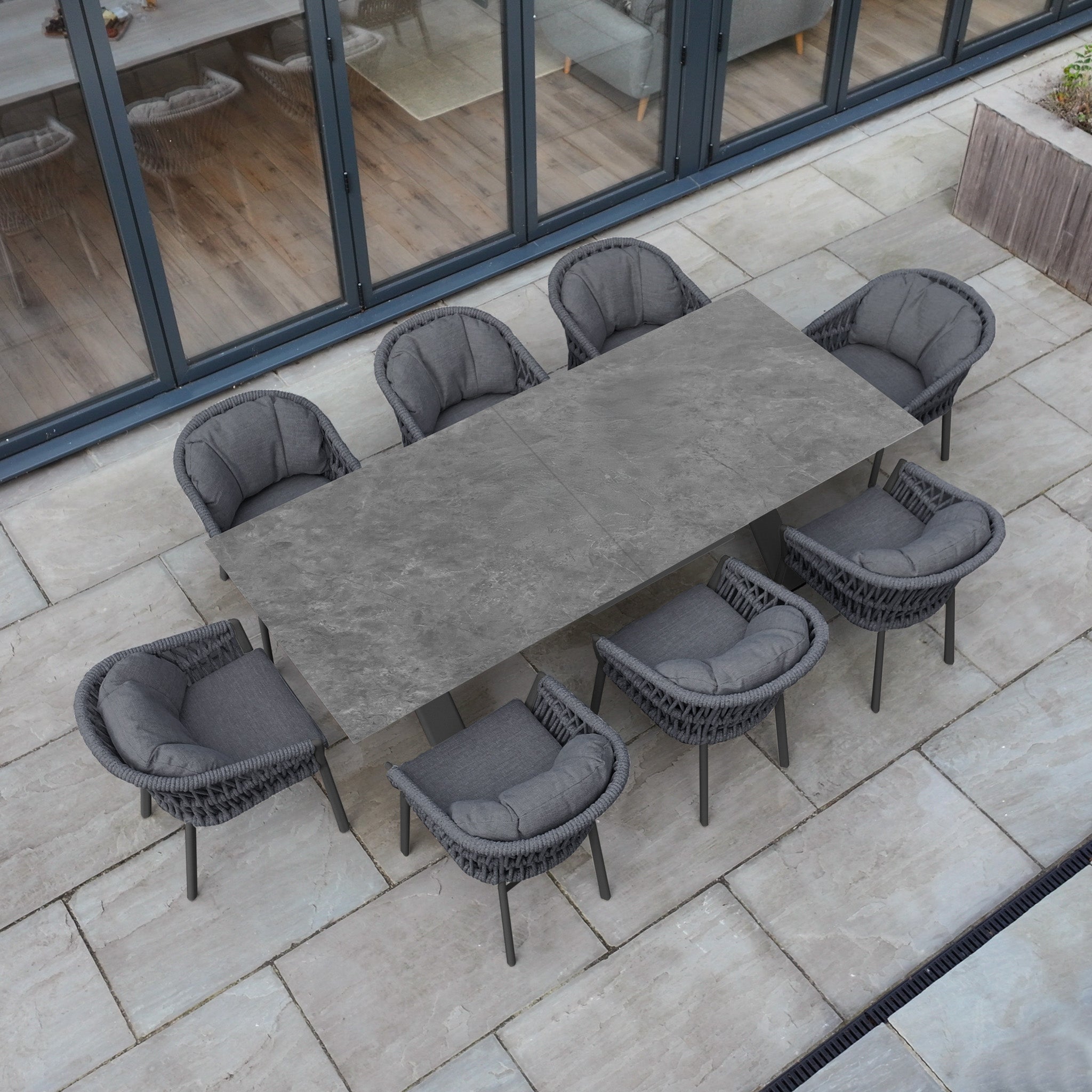 The Pello 8 Seat Dining Set with Albatross Extending Table in Grey features cushioned chairs and a spacious extending table, perfect for outdoor dining on a stylish stone-tiled terrace.