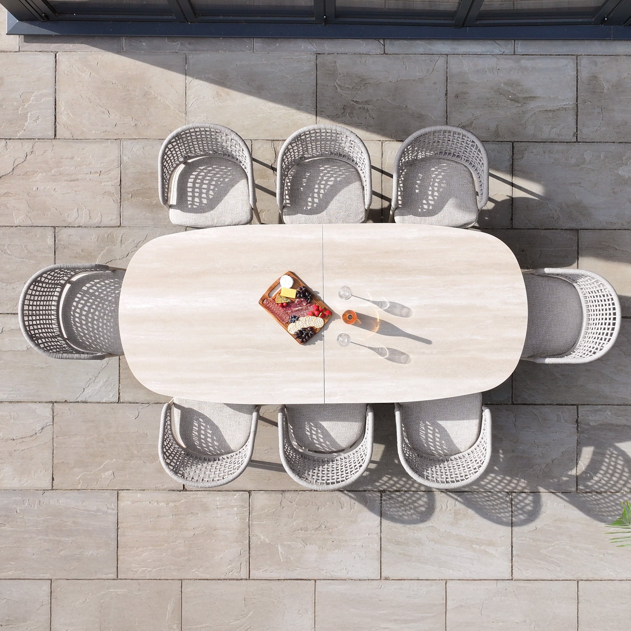 Top view of the Kalama 8 Seat Oval Rope Dining Set with Albatross Extending Table in Oatmeal, featuring six chairs and a small tray of snacks on a tiled patio.