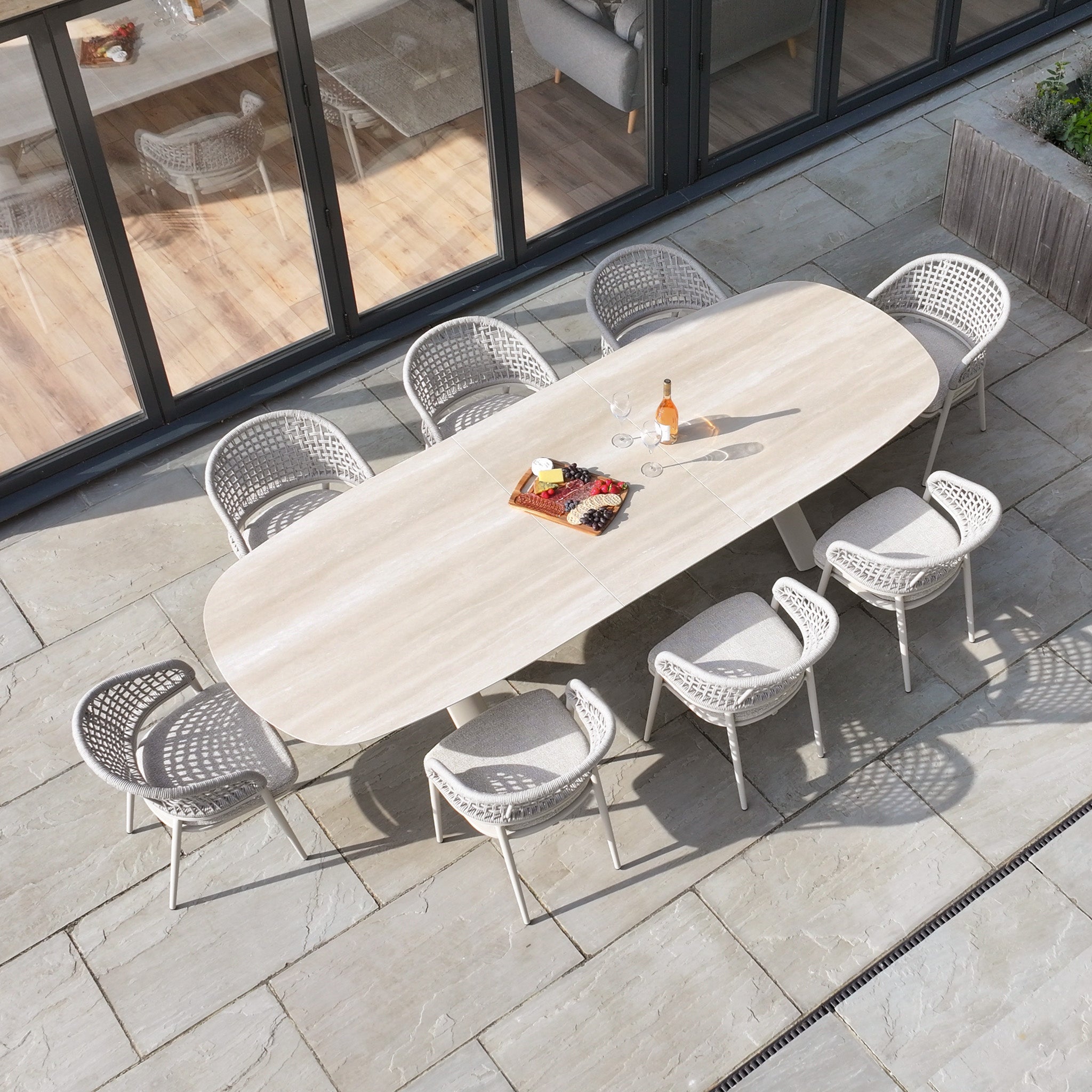 Oval outdoor dining table with eight chairs, wine, and a charcuterie board on a stone patio, just like the Kalama 8 Seat Oval Rope Dining Set with Albatross Extending Table in Oatmeal.