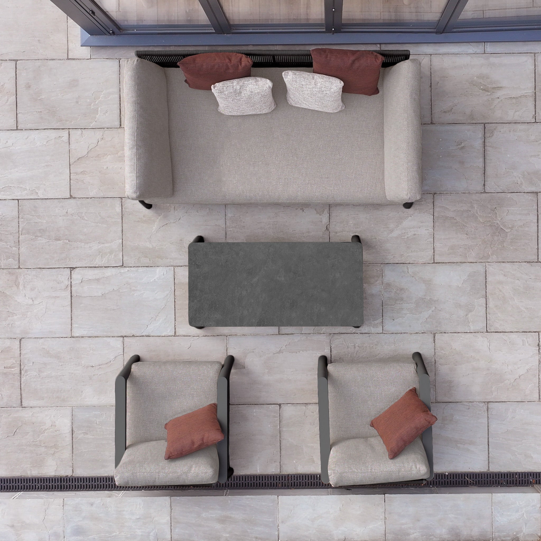The Theia 3 Seat Sofa Set in Truffle, featuring a modular aluminium sofa, two chairs, a coffee table, and cushions, is arranged on a tiled patio floor and viewed from above.
