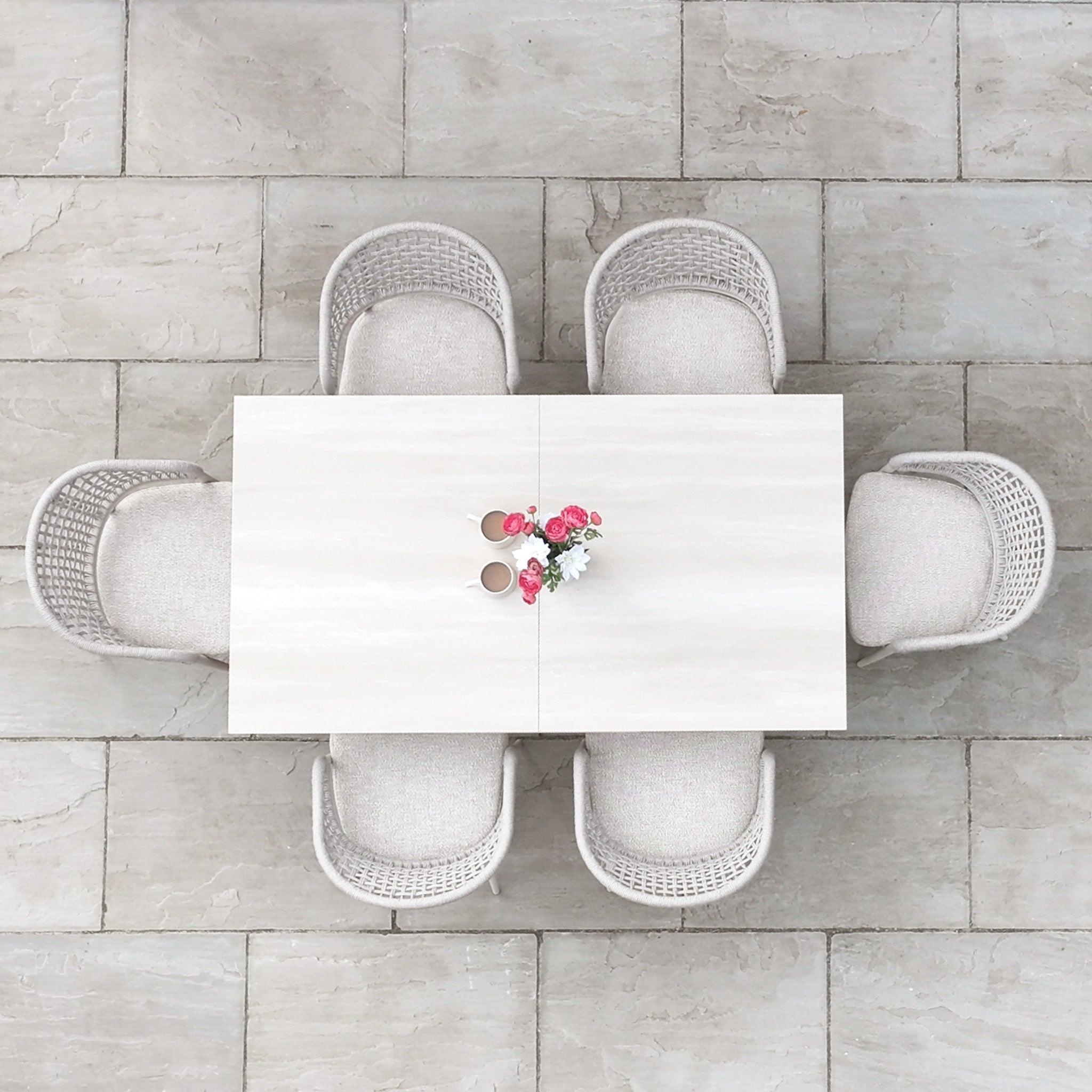 Top view of the Kalama 6 Seat Rope Dining Set with Albatross Extending Table in Oatmeal, featuring six chairs and a small floral centerpiece on a stone-tiled floor.