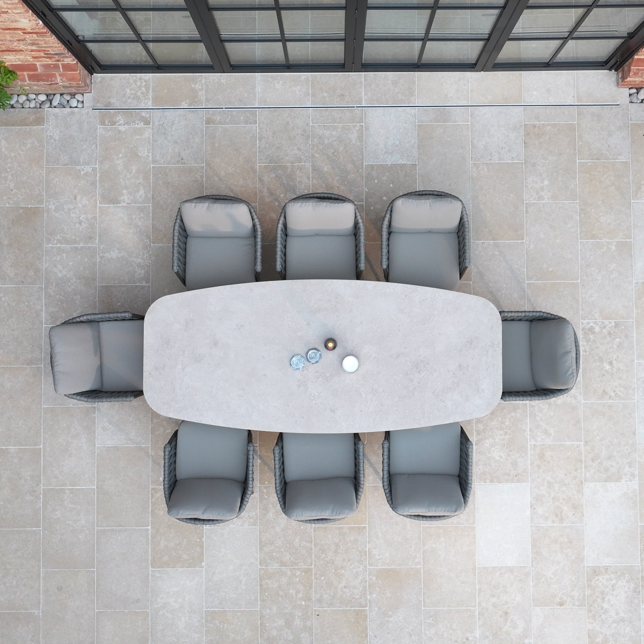 The Capri 8 Seat Curved Rectangular Dining Set in Stone Grey includes a rectangular outdoor table and six cushioned chairs, shown on a stone patio from an overhead view.