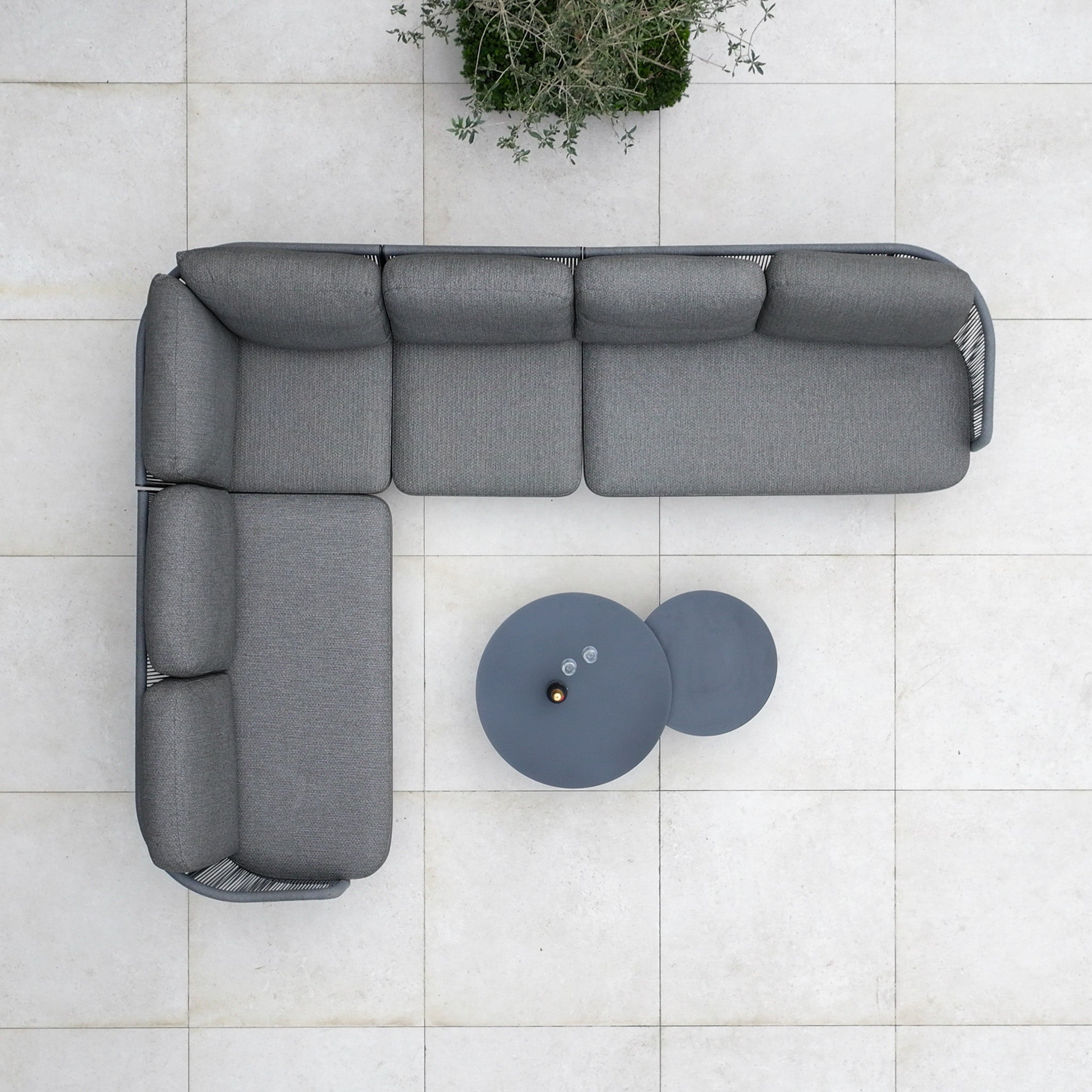 Top view of the Dekota Large Corner Sofa Set in Charcoal, with two round coffee tables on a tiled patio and a potted plant nearby—ideal for creating stylish outdoor spaces.