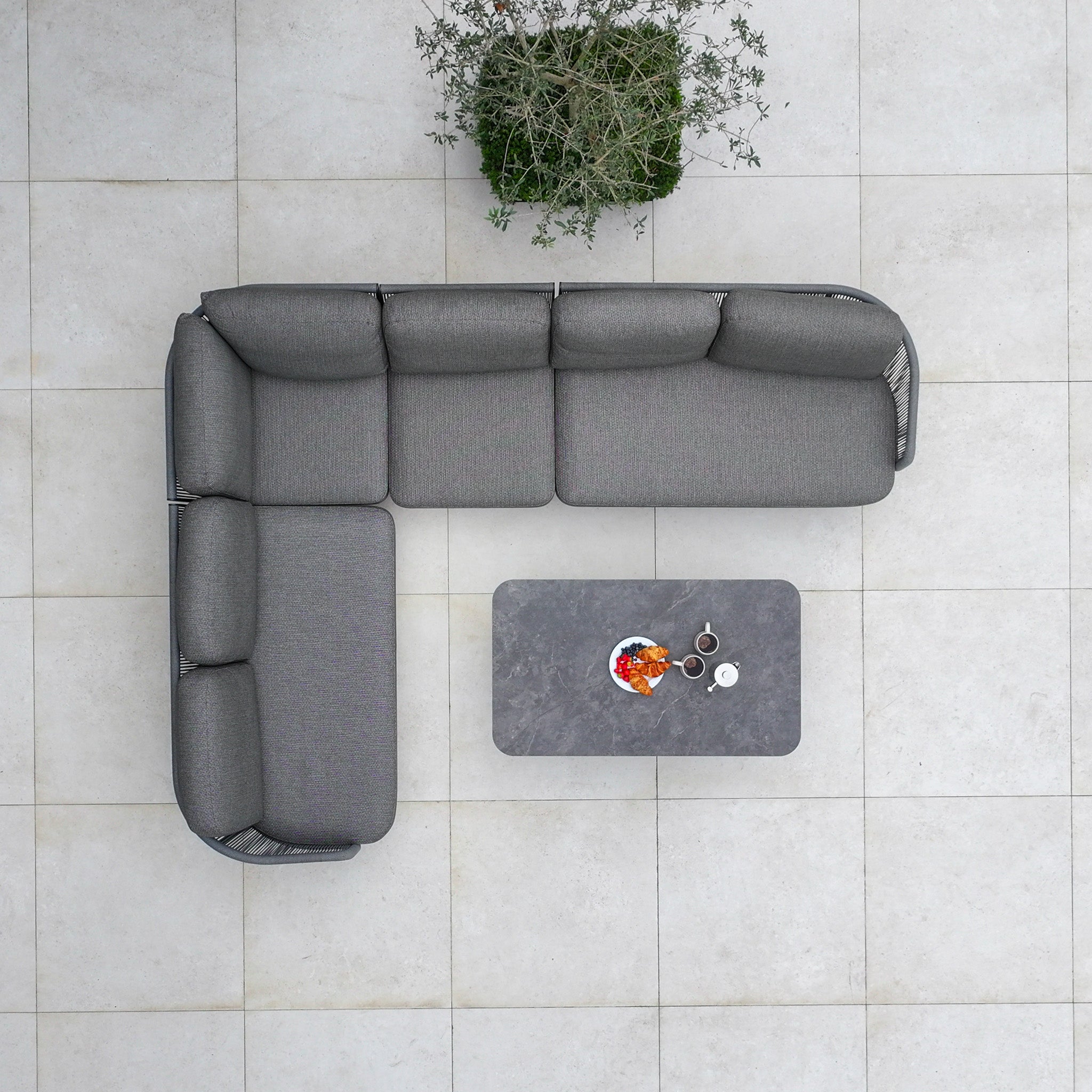 The Dekota Large Corner Sofa Dining Set with Altura Rising Table in Charcoal is shown from above on a tiled floor, arranged in an L-shape with a small plant.